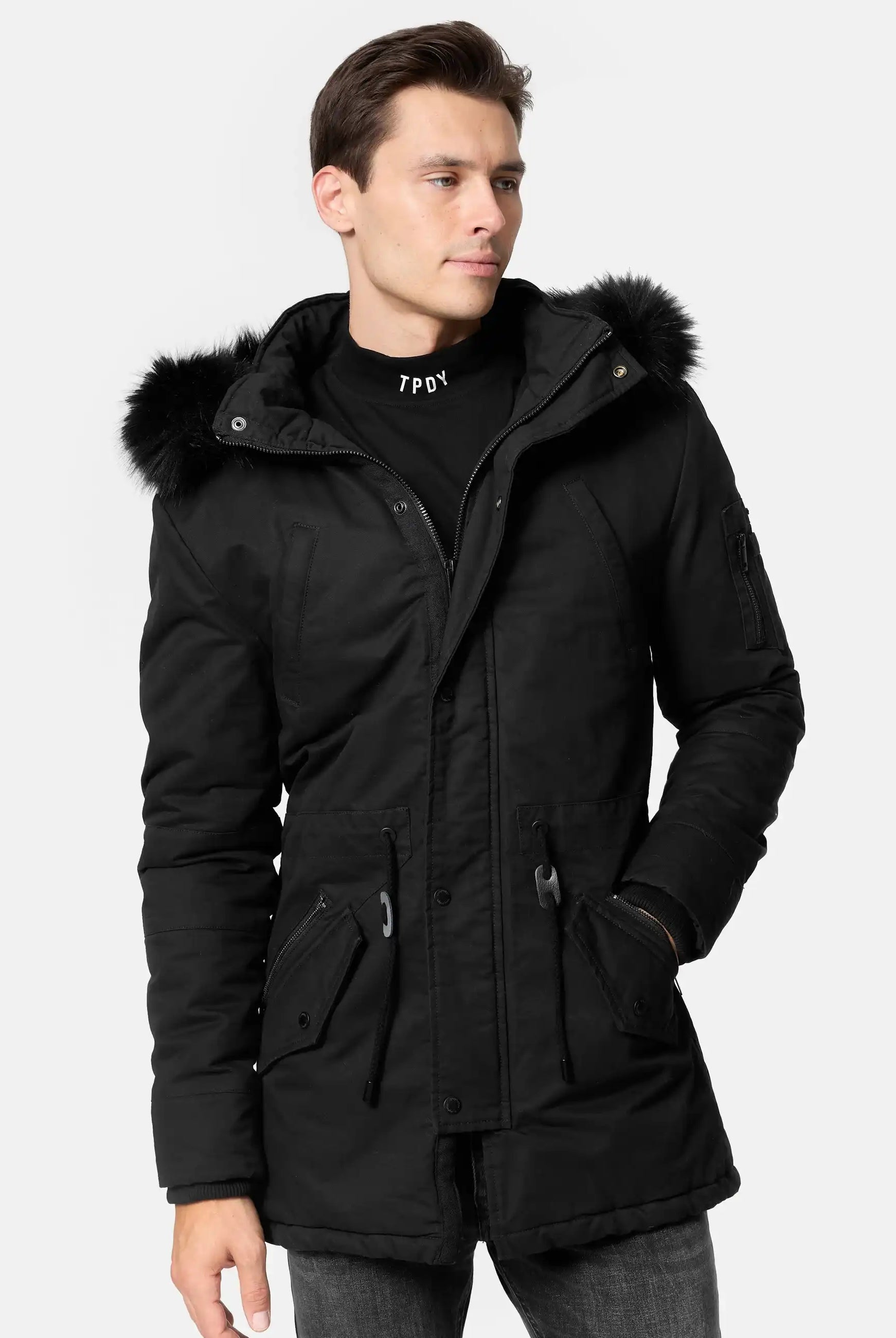 Mann trägt schwarzen TRUEPRODIGY julius Winterparka mit Kunstfellkapuze; Jackendesign: mittellang, mit Tunnelzug und Reißverschlusstaschen; Text auf Pullover: „TPDY“. Ideal für urbane Wintermode.