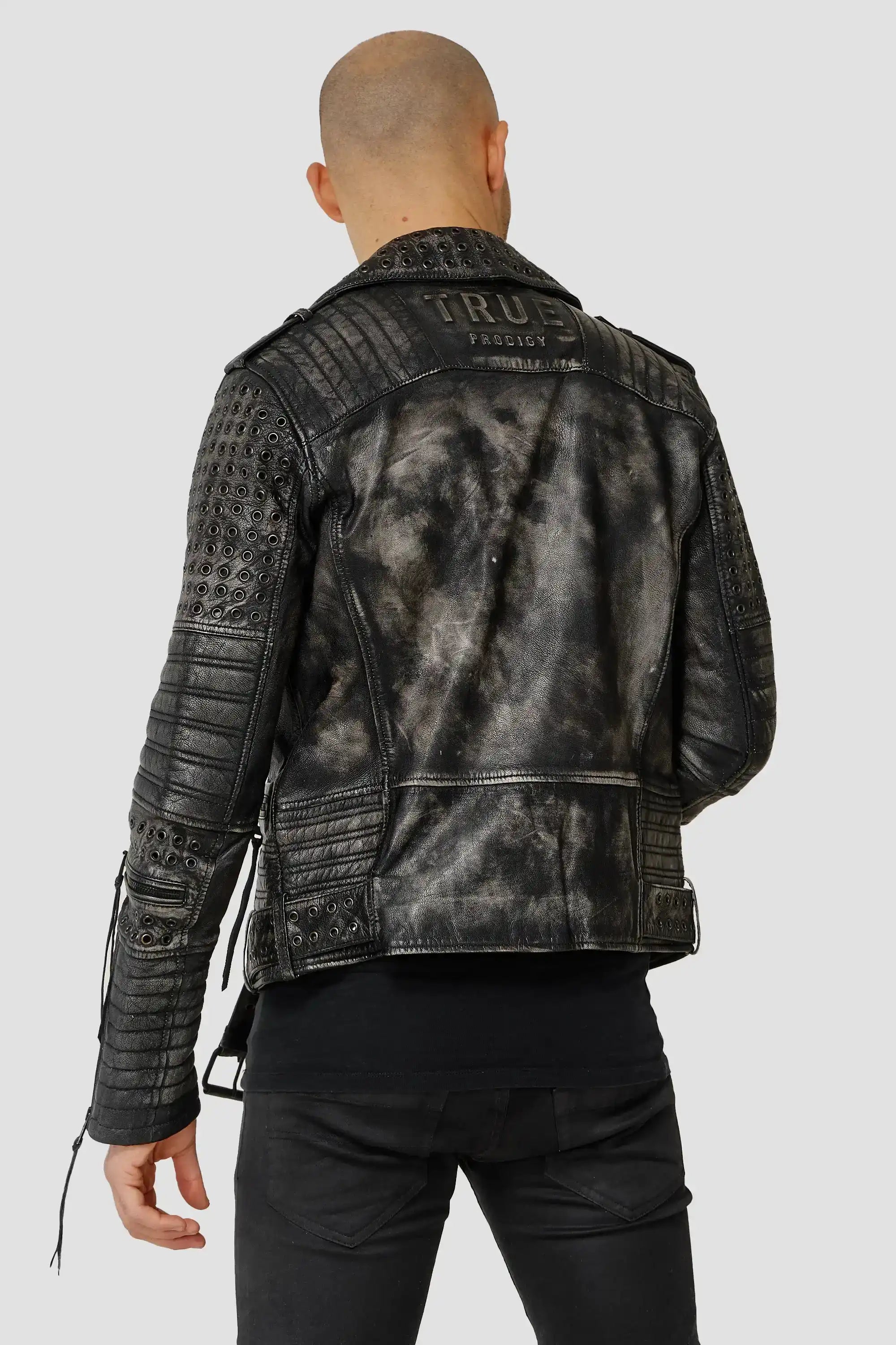 Eine Person trägt die Geralt Vintage Lederjacke mit Ösen von trueprodigy, kombiniert mit schwarzer Hose und Shirt. Die Jacke hat gesteppte und perforierte Details an Ärmeln und Schultern, die Person ist von hinten zu sehen, der Kopf kahl.