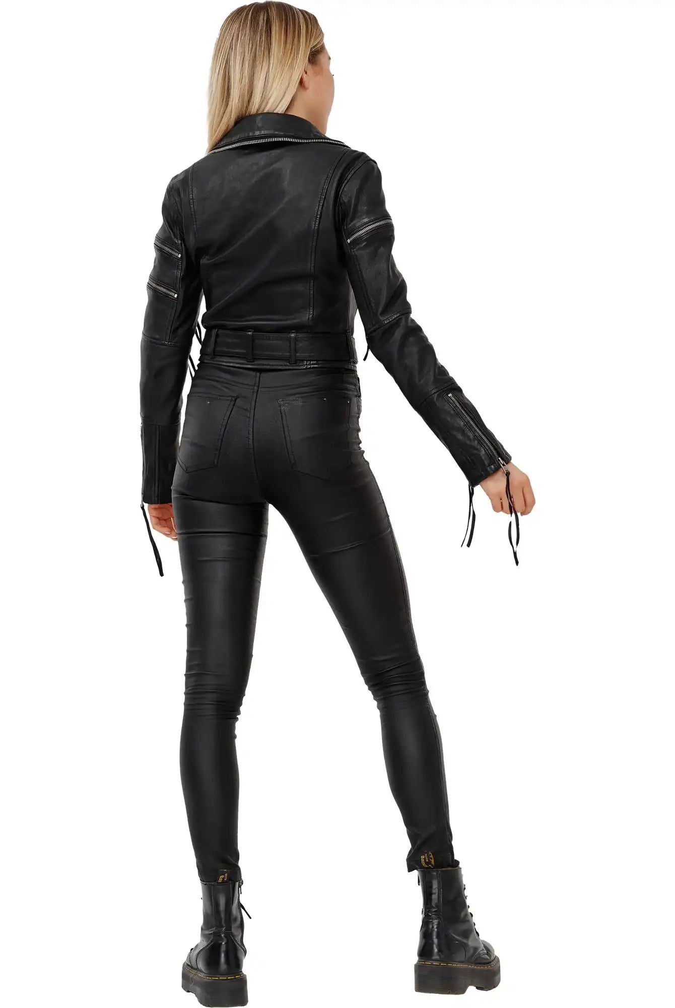 Eine Person mit langen blonden Haaren, von hinten gesehen, trägt die Izzy Bikerlederjacke mit Gürtel von trueprodigy, schwarze Skinny-Hosen und schwarze Schnürstiefel und steht vor einem schlichten weißen Hintergrund.