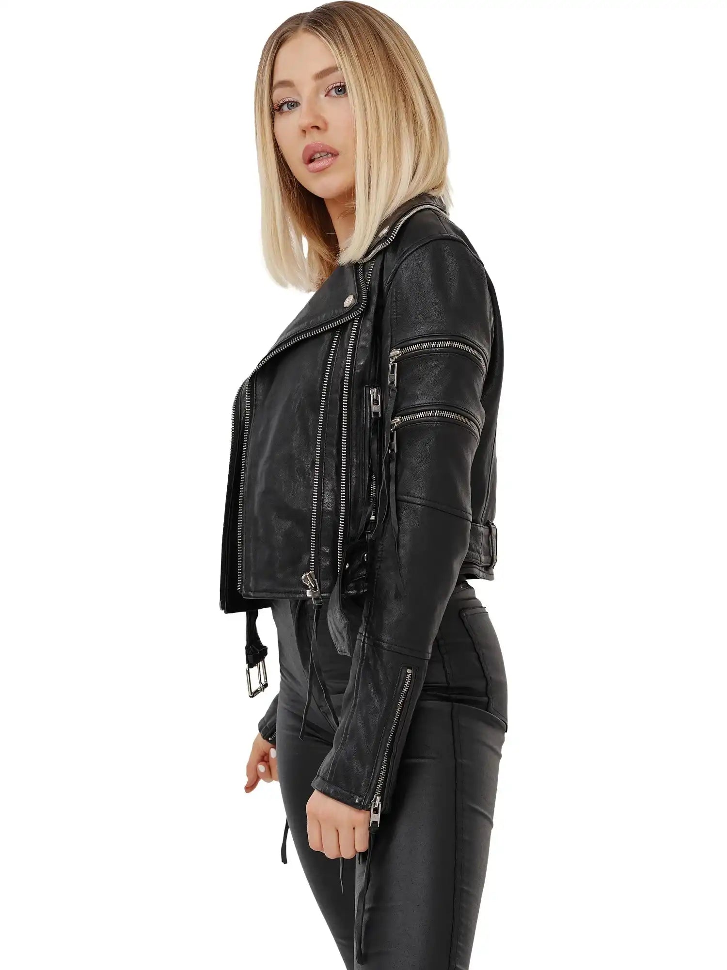 Eine Frau mit glattem blondem Haar trägt die trueprodigy Izzy Bikerlederjacke mit Gürtel und schwarzer Hose. Sie steht seitlich und schaut in die Kamera vor einem weißen Hintergrund.