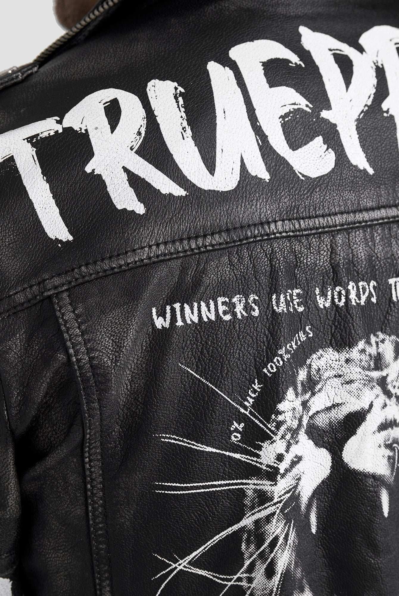 Nahaufnahme der Russell Lederjacke mit Print von trueprodigy: schwarzes Ziegenleder, fetter weißer "TRUEPR" und "WINNERS USE WORDS THAT..." Text über einer brüllenden Löwengrafik, mit kantigen weißen Farbspritzern für einen echten Biker-Look.