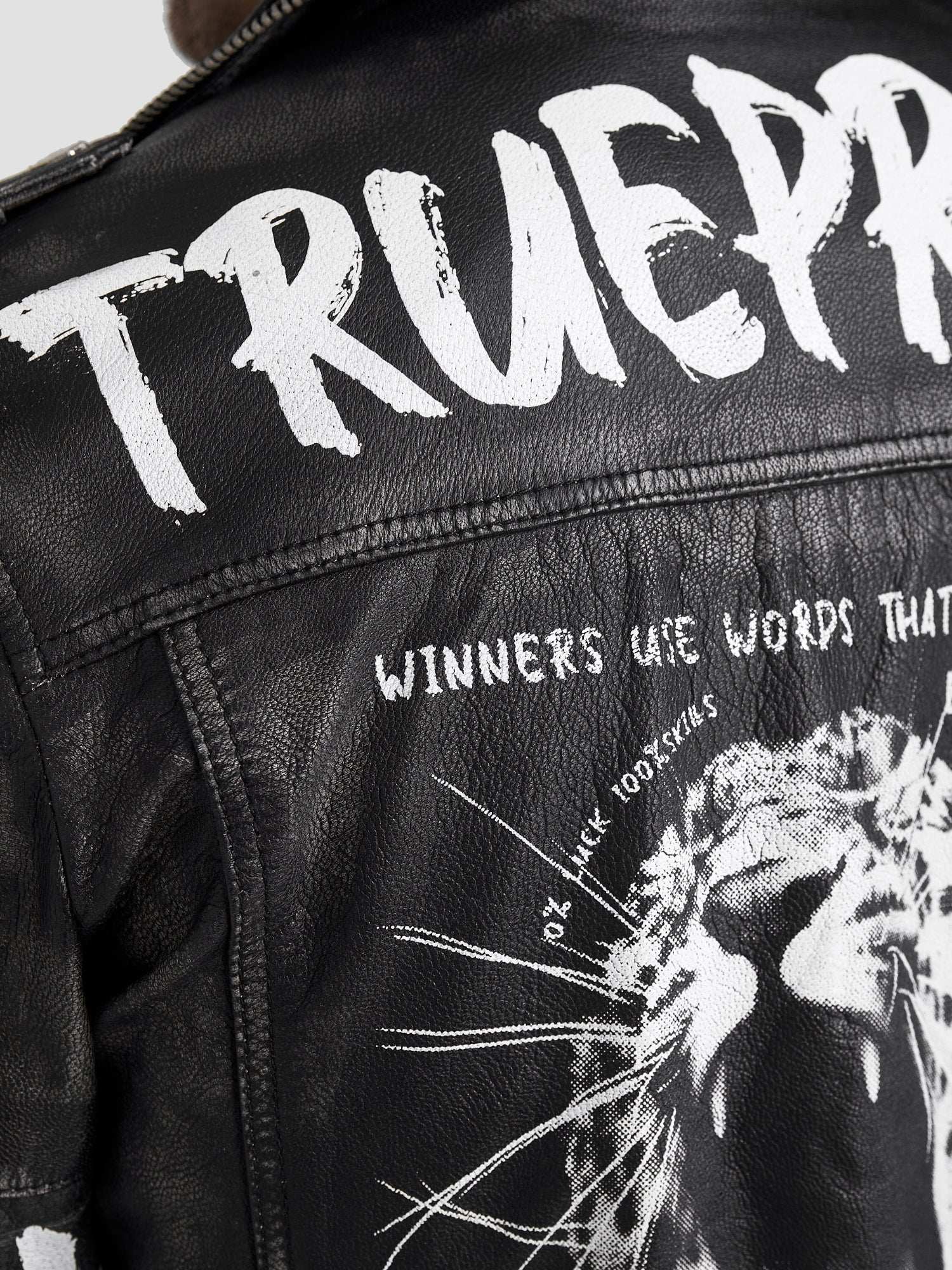 Nahaufnahme der Russell Lederjacke mit Print von trueprodigy: schwarzes Ziegenleder, fetter weißer "TRUEPR" und "WINNERS USE WORDS THAT..." Text über einer brüllenden Löwengrafik, mit kantigen weißen Farbspritzern für einen echten Biker-Look.
