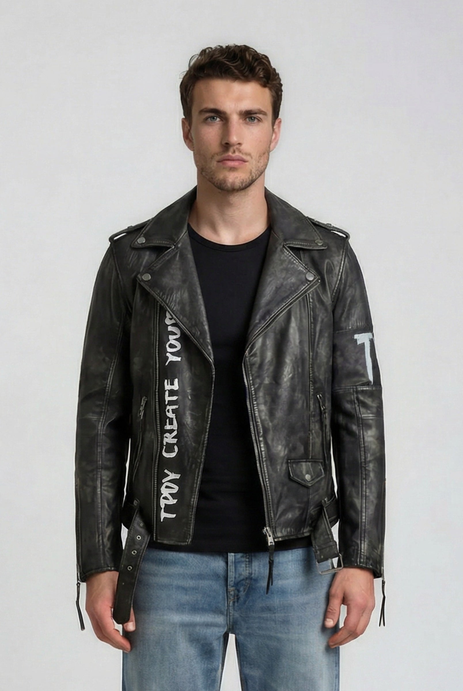 Ein Mann trägt die trueprodigy Biker Lederjacke Herren "Russell" mit Rücken-Print, dazu ein schwarzes T-Shirt und blaue Jeans, und steht vor einem schlichten, hellen Hintergrund.