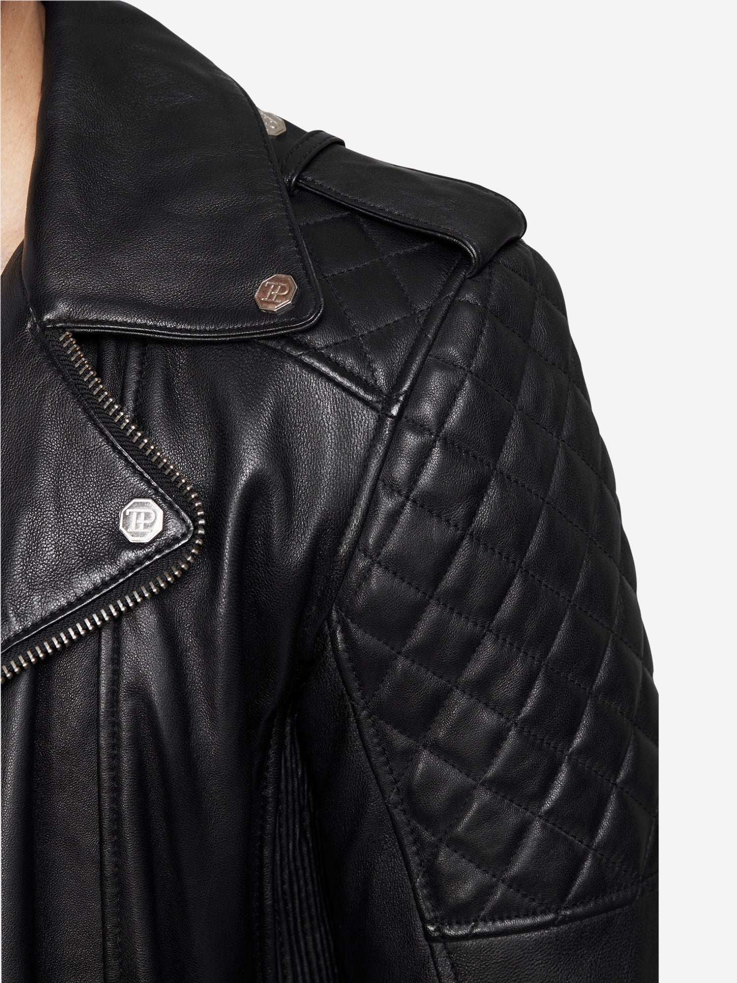 Nahaufnahme einer trueprodigy Simba Bikerlederjacke mit Gürtel, mit gesteppten Schulternähten, silbernen Druckknöpfen und einem sichtbaren Reißverschluss. Das Foto konzentriert sich auf die obere Brust und die Schulter des Trägers.