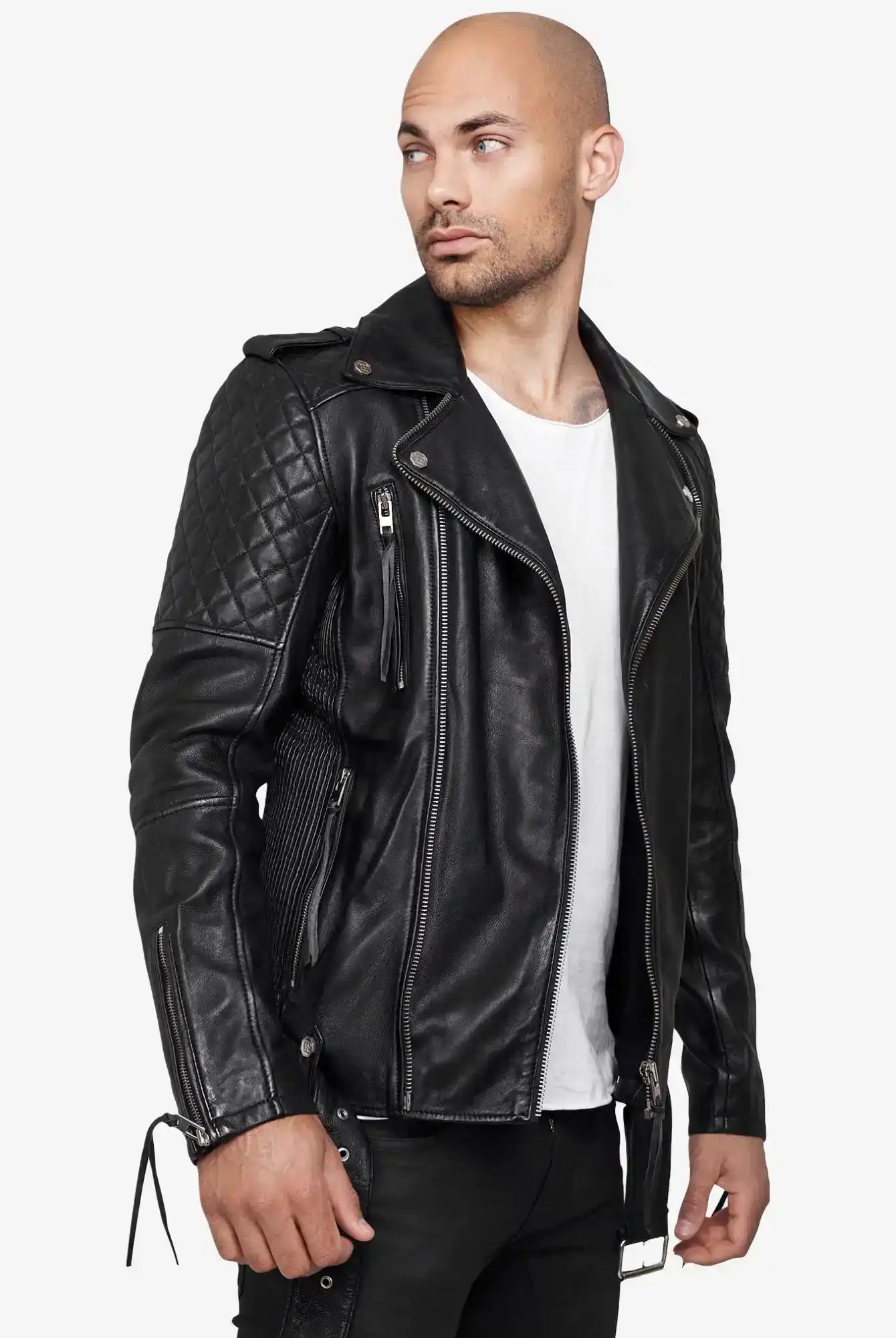 Ein Mann mit rasiertem Kopf trägt eine trueprodigy Simba Bikerlederjacke mit Gürtel über einem weißen T-Shirt und einer schwarzen Hose, steht vor einem hellen Hintergrund und schaut zur Seite.