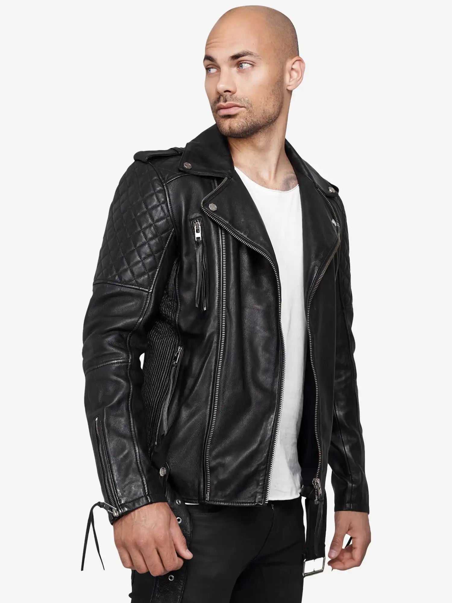 Ein Mann mit rasiertem Kopf trägt eine trueprodigy Simba Bikerlederjacke mit Gürtel über einem weißen T-Shirt und einer schwarzen Hose, steht vor einem hellen Hintergrund und schaut zur Seite.