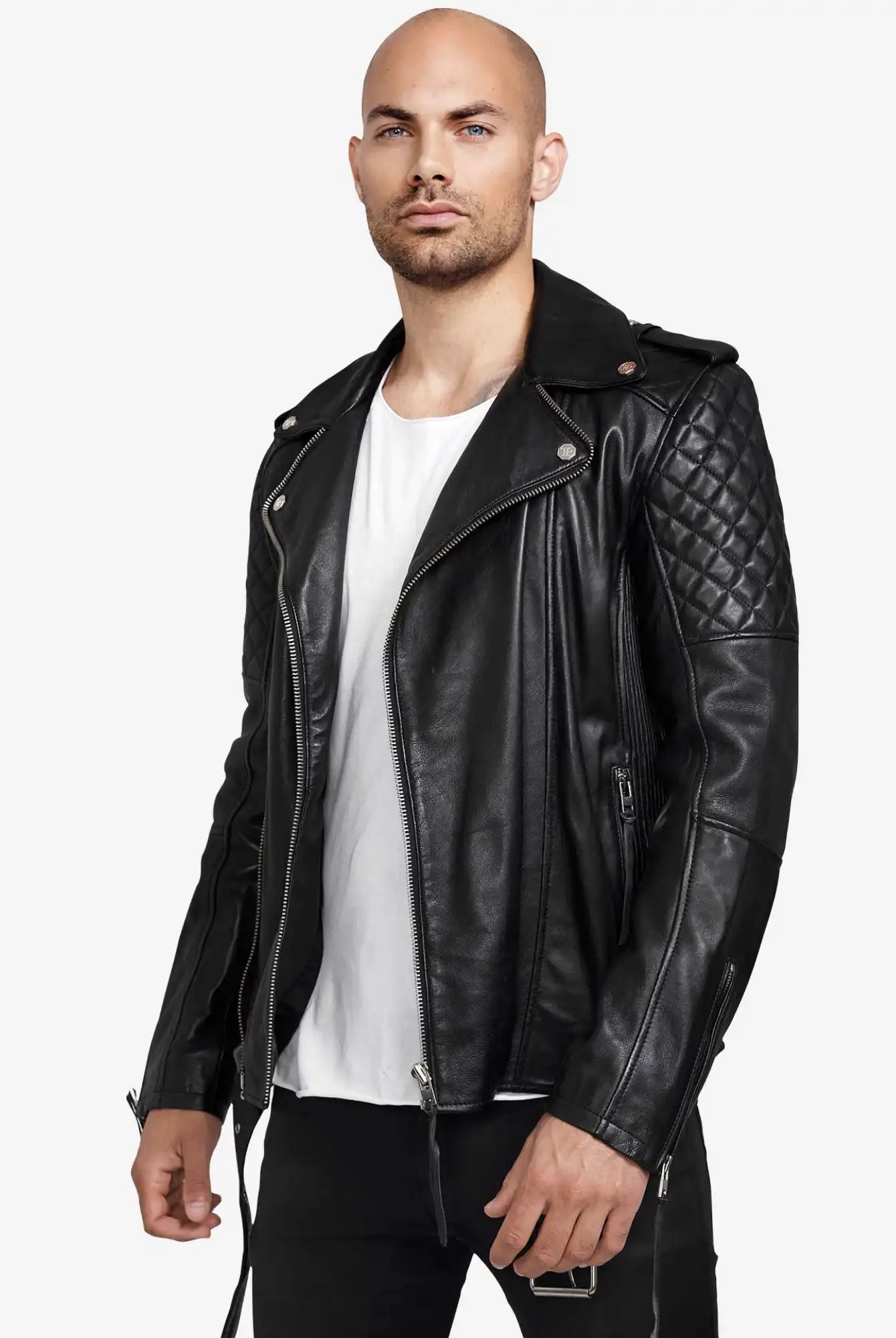 Ein Mann mit rasiertem Kopf und kurzem Bart trägt die trueprodigy Simba Bikerlederjacke mit Gürtel in Schwarz über einem weißen T-Shirt und einer schwarzen Hose und steht selbstbewusst vor einem hellen Hintergrund, um diese stilvolle Herrenjacke zu präsentieren.