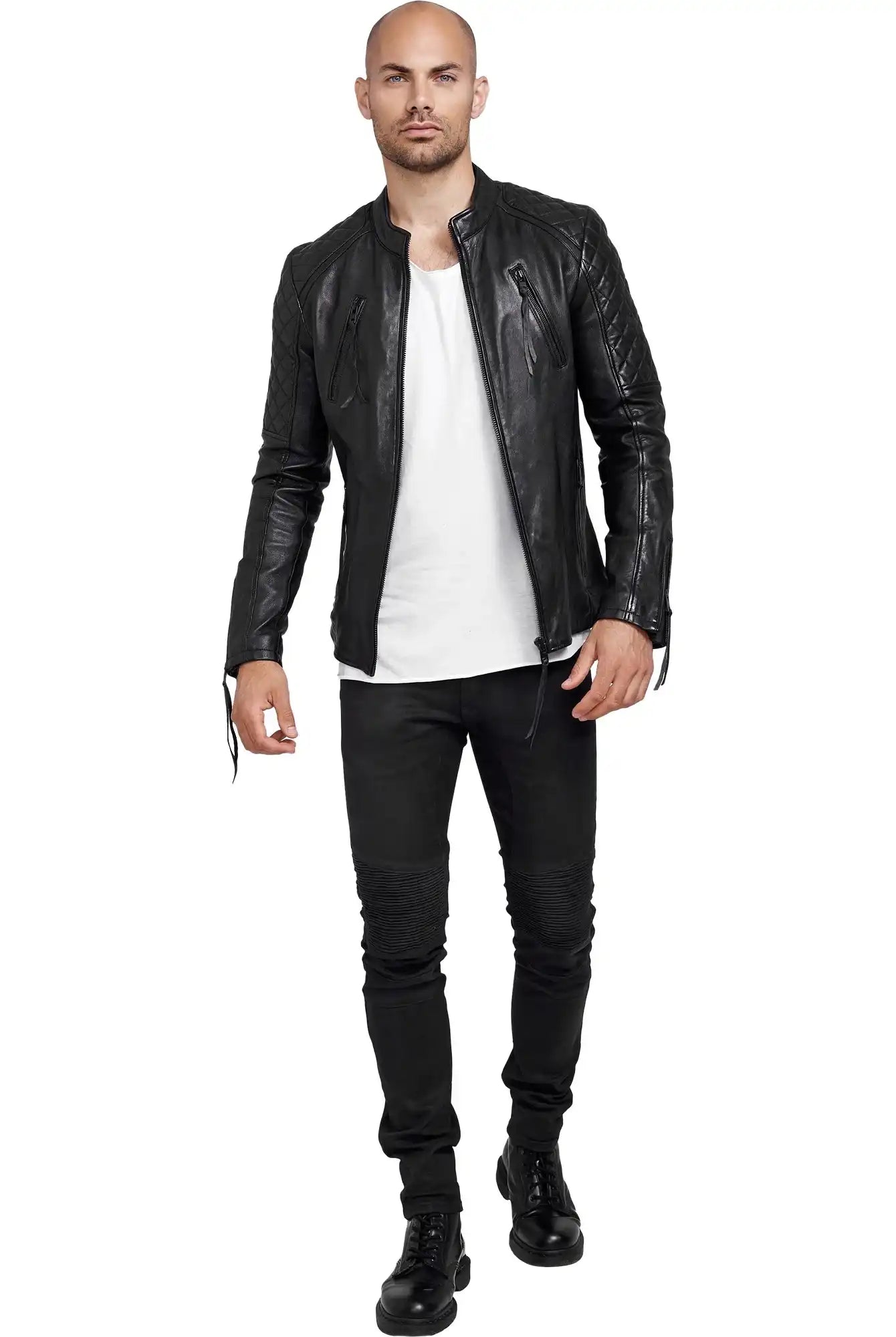 Ein Mann mit rasiertem Kopf, der eine Trueprodigy Simba Bikerlederjacke mit Gürtel, ein weißes T-Shirt, schwarze Jeans und schwarze Stiefel trägt, steht vor einem weißen Hintergrund.