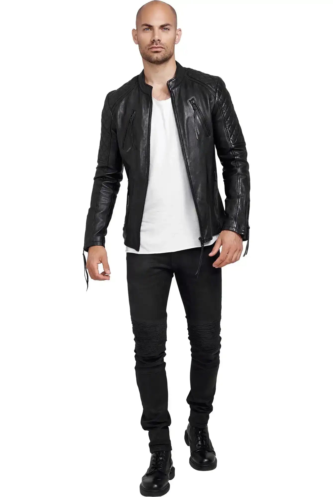 Ein Mann mit rasiertem Kopf, der eine Trueprodigy Simba Bikerlederjacke mit Gürtel, ein weißes T-Shirt, schwarze Jeans und schwarze Stiefel trägt, steht vor einem weißen Hintergrund.