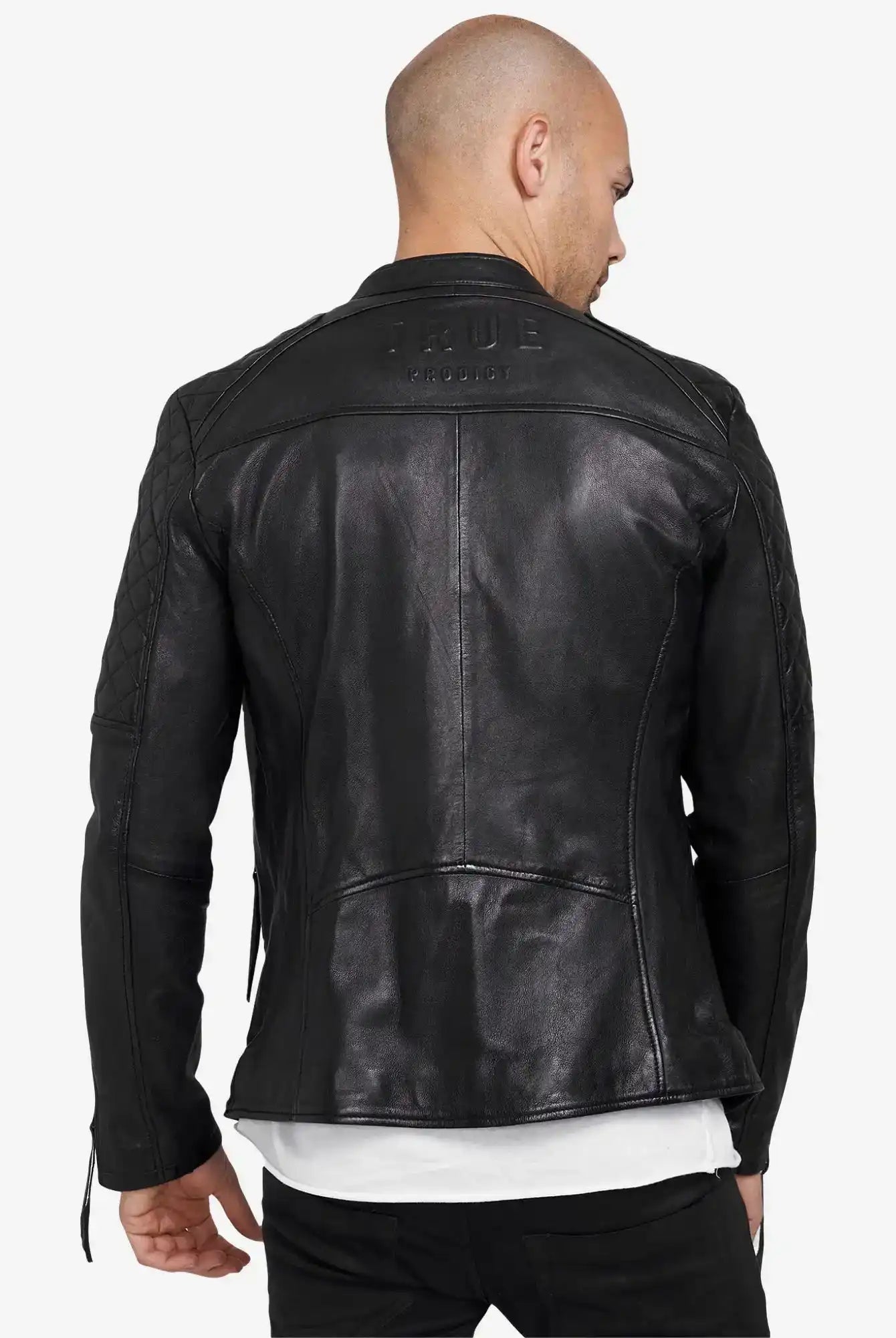 Von hinten ist eine Person mit rasiertem Kopf zu sehen, die eine schwarze Franky Lederjacke mit Stehkragen von trueprodigy mit gesteppten Ärmeln und Schultern, dem eingeprägten Markennamen auf dem oberen Rücken, und einem weißen Hemd darunter trägt.