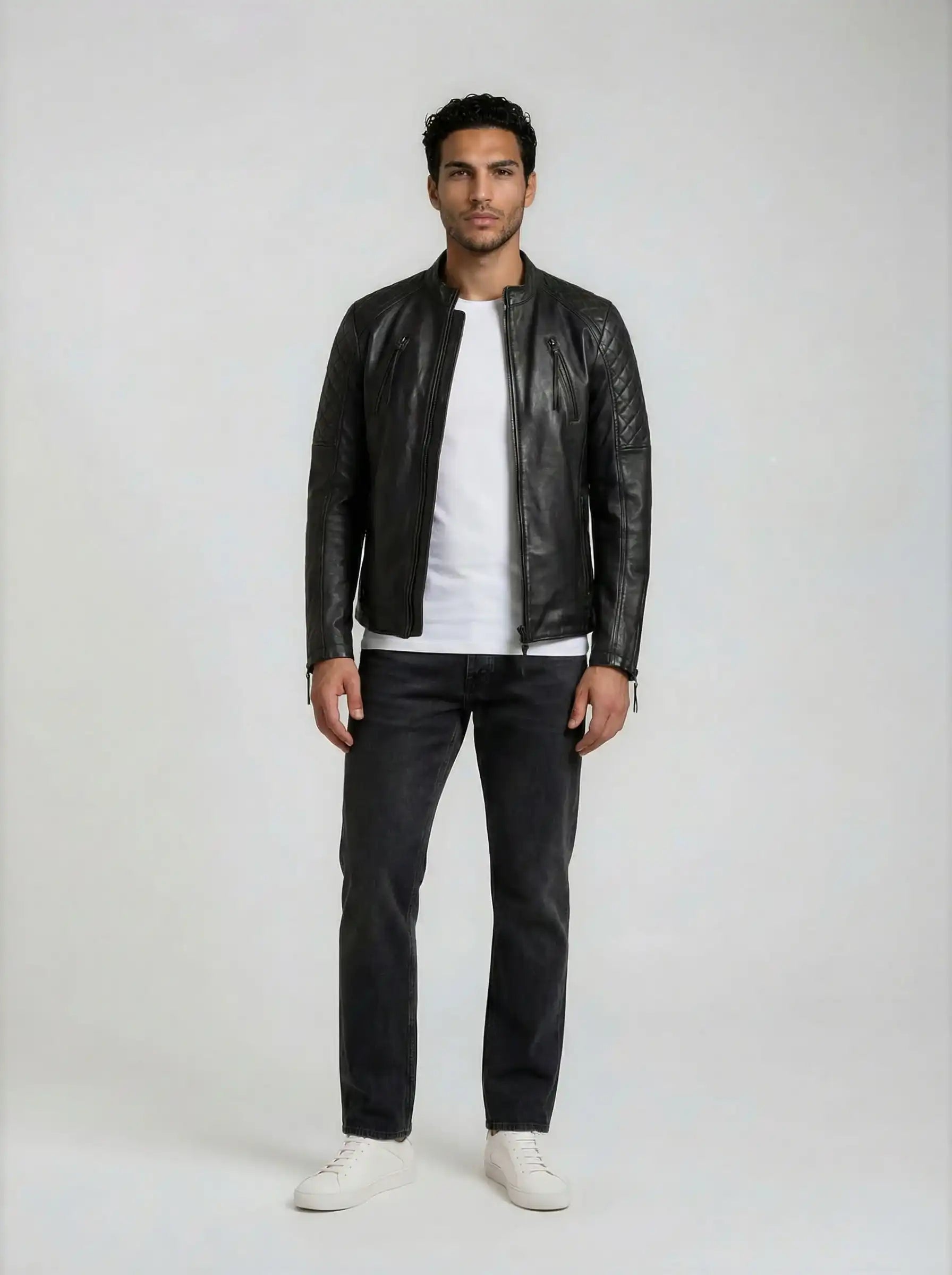 Ein Mann schaut nach vorne und trägt die trueprodigy Racing Lederjacke Herren "Franky" mit Rautensteppung, gestylt mit weißem T-Shirt, dunkler Jeans und weißen Turnschuhen vor einem schlichten hellen Hintergrund.
