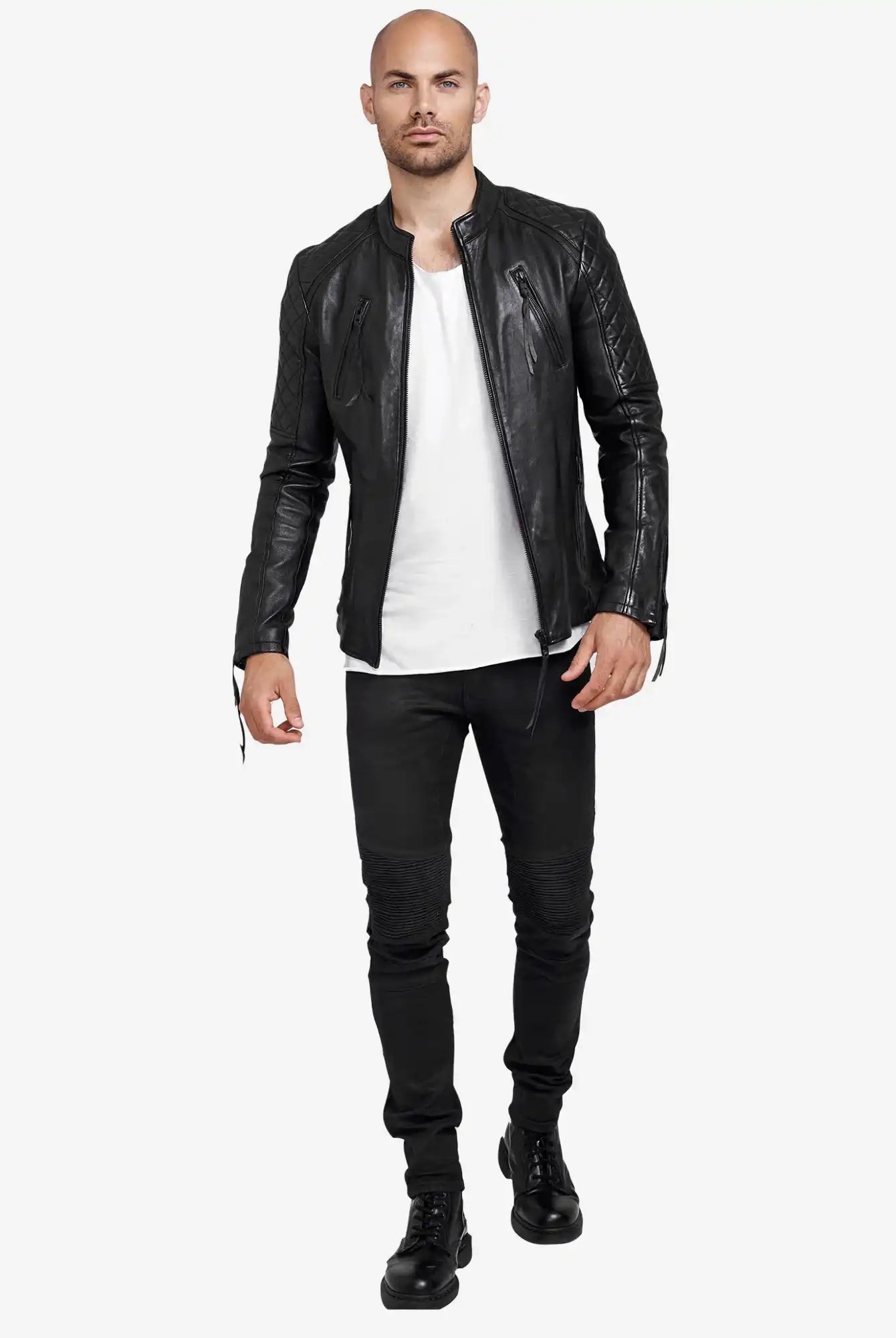 Ein Mann steht frontal, trägt die trueprodigy Franky Lederjacke mit Stehkragen, ein weißes T-Shirt, schwarze Jeans und Boots. Er ist kahlköpfig, hat kurzen Bart und einen neutralen Gesichtsausdruck mit leicht erhobener Hand.