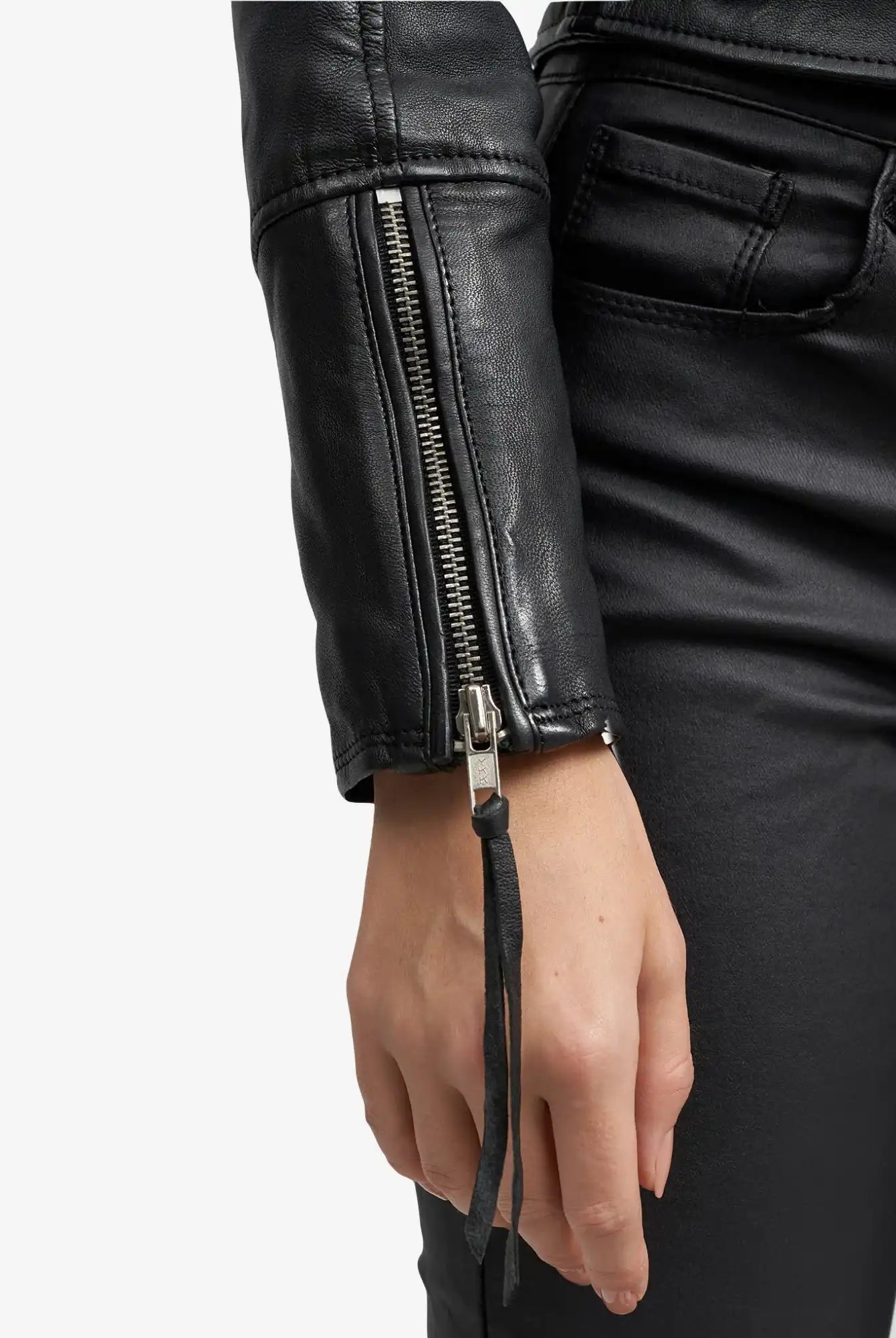 Eine Person trägt eine schwarze Hose und die trueprodigy Laila Lederjacke mit Druck, die mit ihrem schicken silbernen Ärmelreißverschluss für einen echten Trend-Look sorgt. Der lässige linke Arm unterstreicht dieses stylische Detail der Jacke.