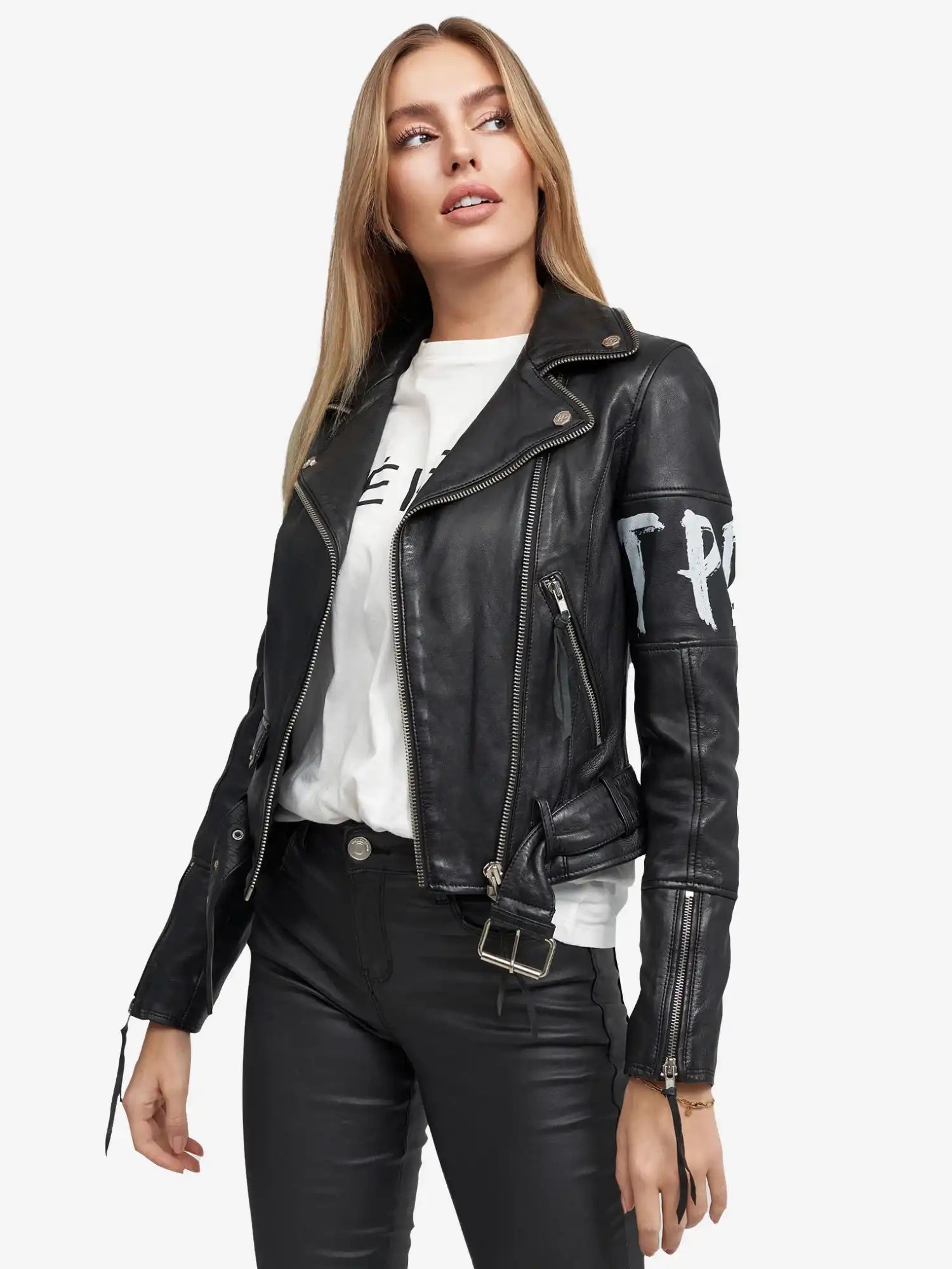 Eine Frau mit langen blonden Haaren trägt die trueprodigy Laila Lederjacke mit Druck über einem weißen Grafik-T-Shirt und einer schwarzen Hose, steht leicht links und schaut zur Seite.
