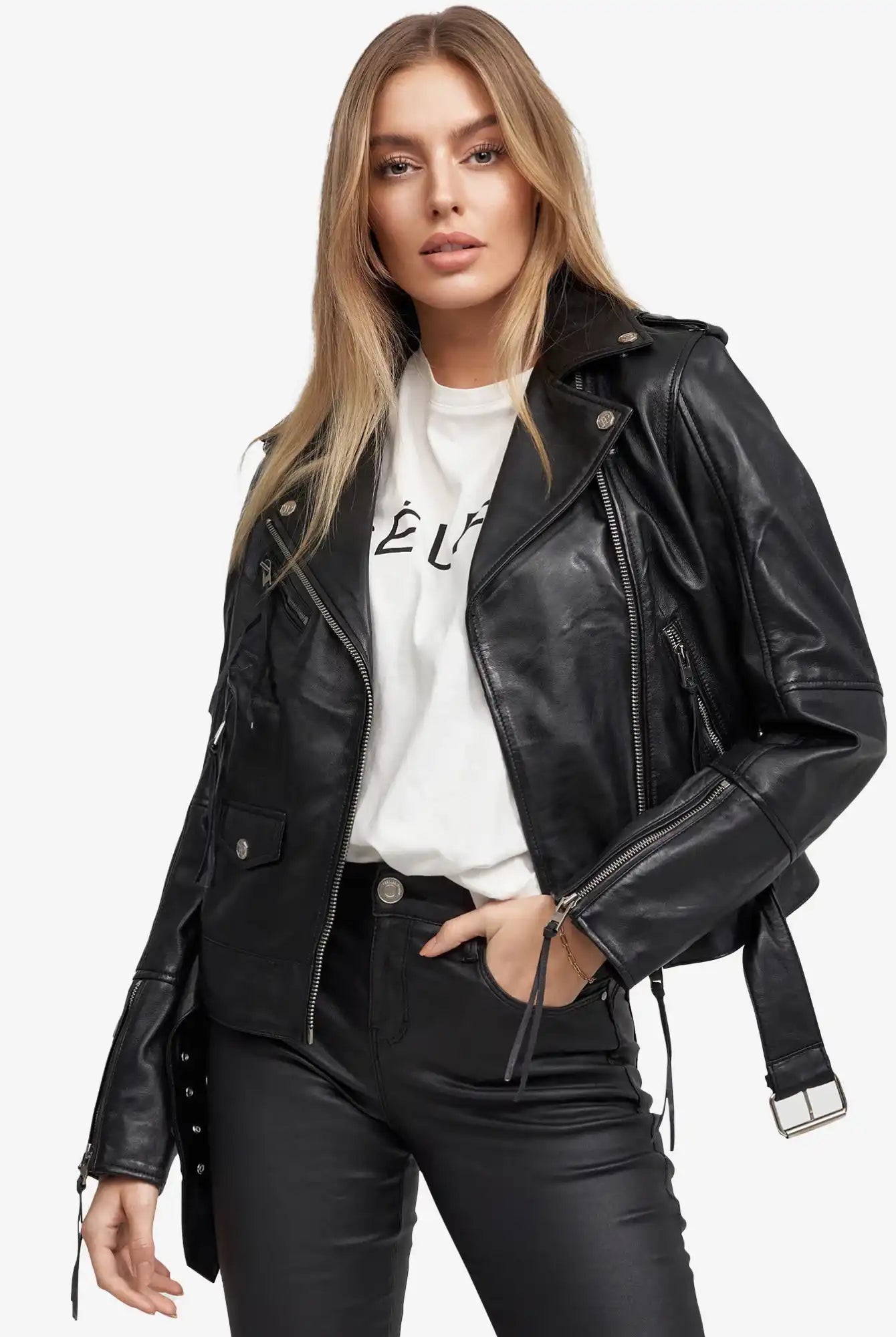 Eine Frau mit langen blonden Haaren trägt die trueprodigy Milena Lederjacke mit Gürtel-eine schwarze Damen-Lederjacke-über einem weißen T-Shirt mit schwarzem Text und schwarzen Hosen vor weißem Hintergrund.