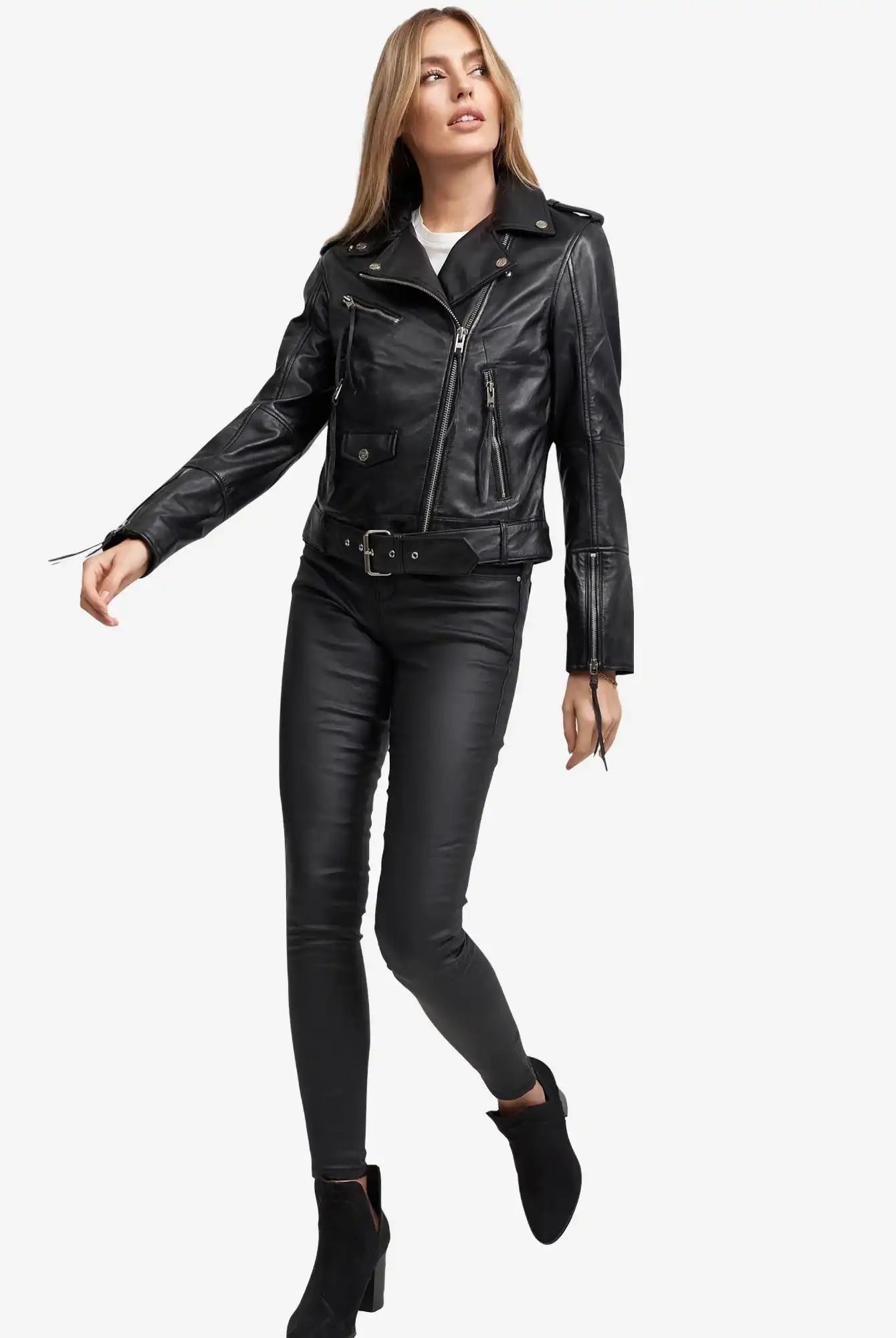 Eine Frau trägt die Milena Lederjacke mit Gürtel von trueprodigy mit schwarzer, taillierter Hose und Stiefeletten und steht vor einem weißen Hintergrund. Sie hat lange blonde Haare, blickt zur Seite und streckt einen Arm aus.