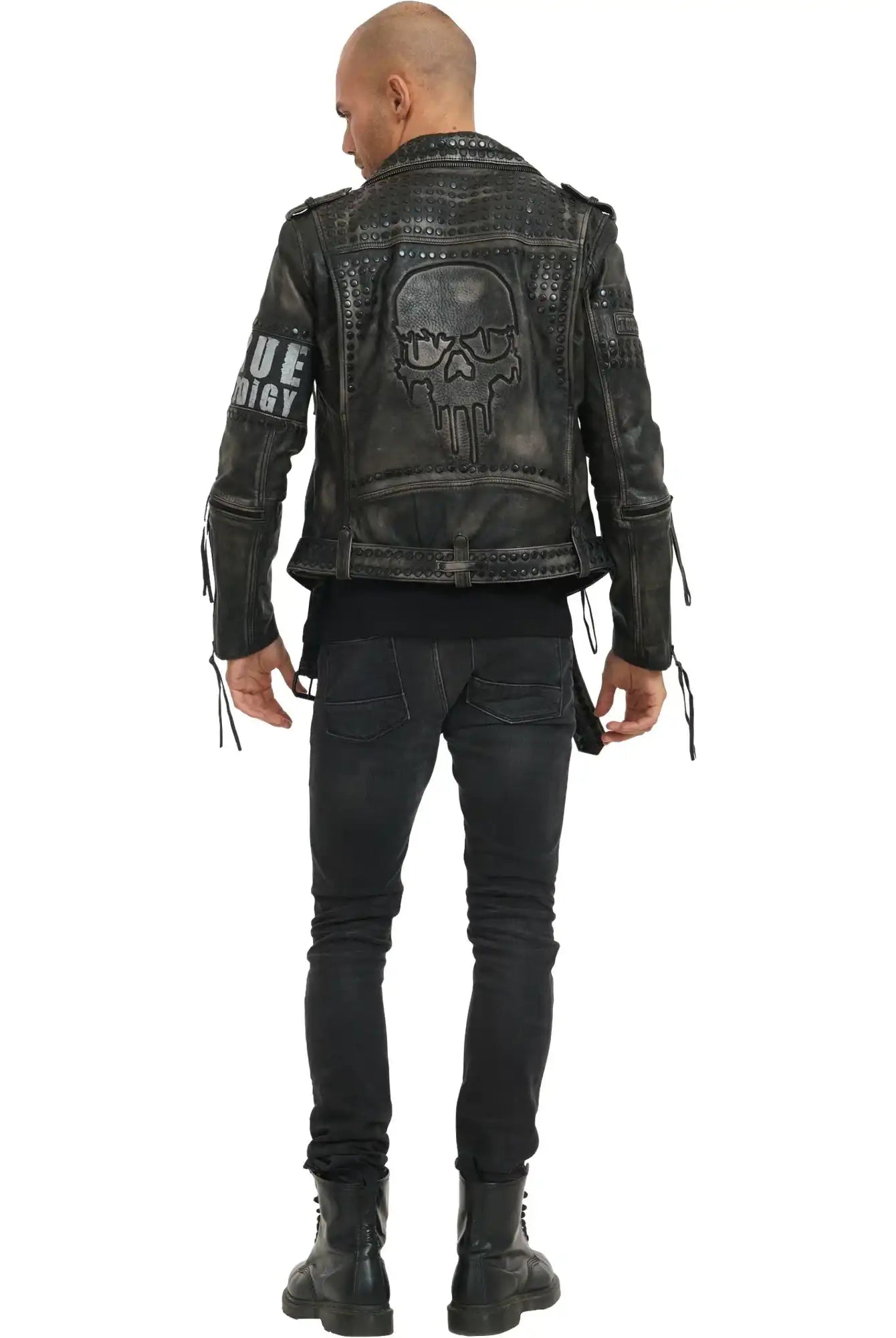 Eine Person steht mit dem Gesicht zur Wand und trägt die trueprodigy Dwayne Lederjacke mit Nieten und Druck im Biker-Look, mit großem Totenkopf-Print auf dem Rücken, Nieten und Ärmelreißverschlüssen, gepaart mit schwarzen Jeans und Stiefeln. Textdetails akzentuieren die kantige Jacke.