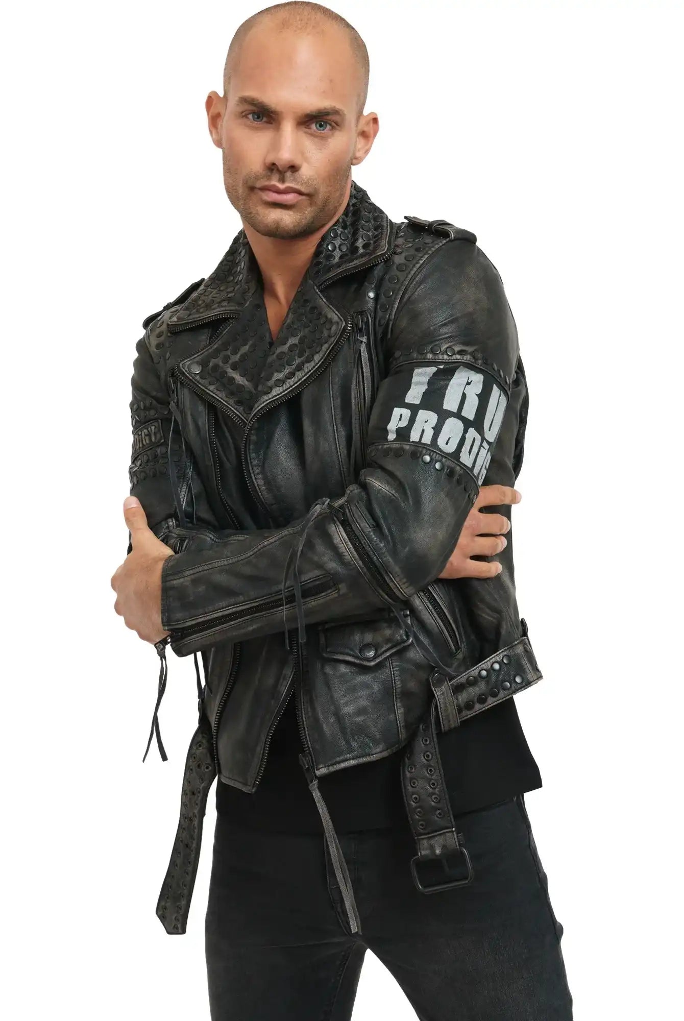 Ein Mann mit rasiertem Kopf und gestutztem Bart rockt im Biker-Look, trägt die trueprodigy Dwayne Lederjacke mit Nieten und Druck und eine schwarze Hose. Er steht mit verschränkten Armen vor einem weißen Hintergrund und schaut in die Kamera.
