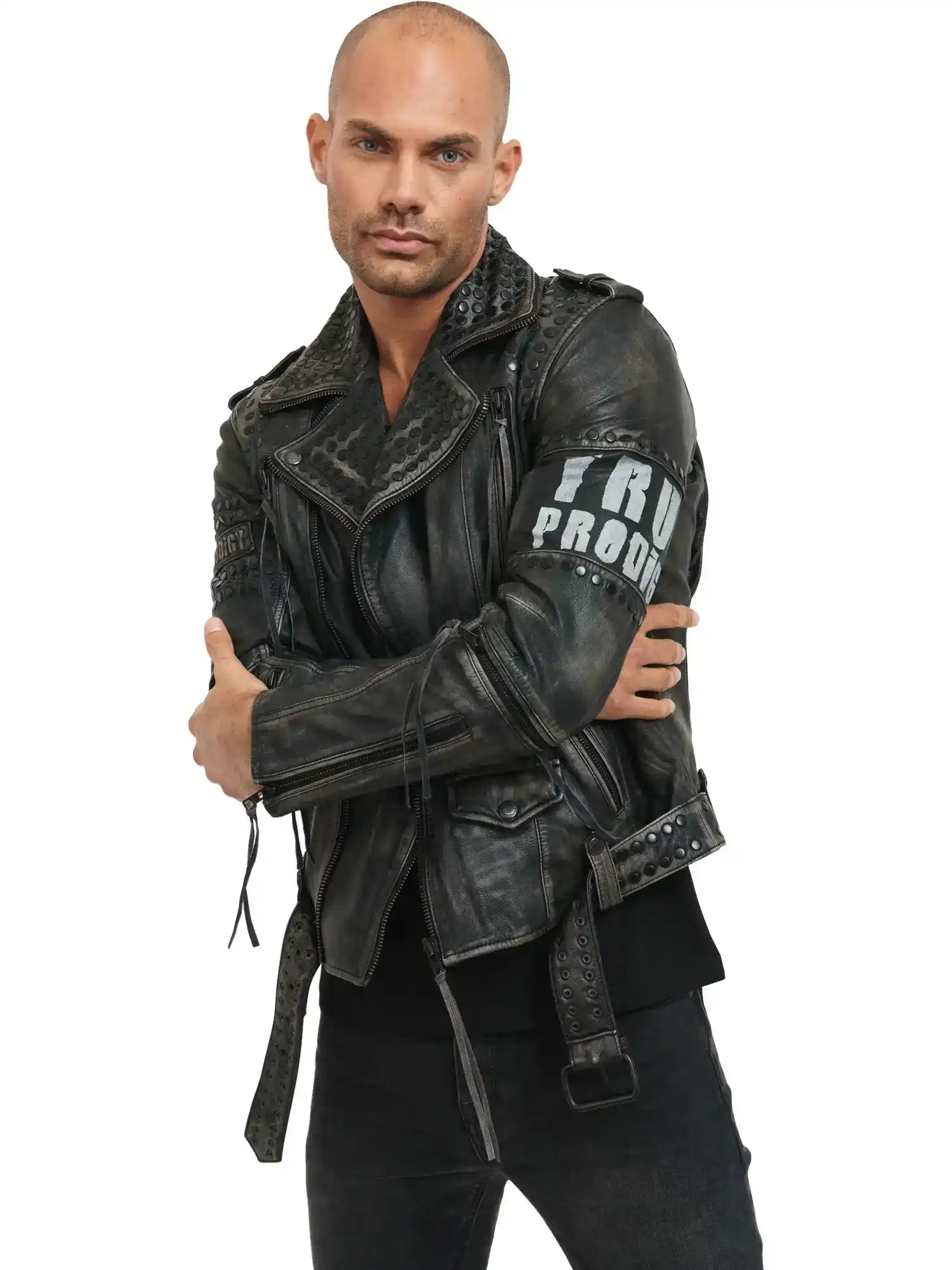 Ein Mann mit rasiertem Kopf und gestutztem Bart rockt im Biker-Look, trägt die trueprodigy Dwayne Lederjacke mit Nieten und Druck und eine schwarze Hose. Er steht mit verschränkten Armen vor einem weißen Hintergrund und schaut in die Kamera.