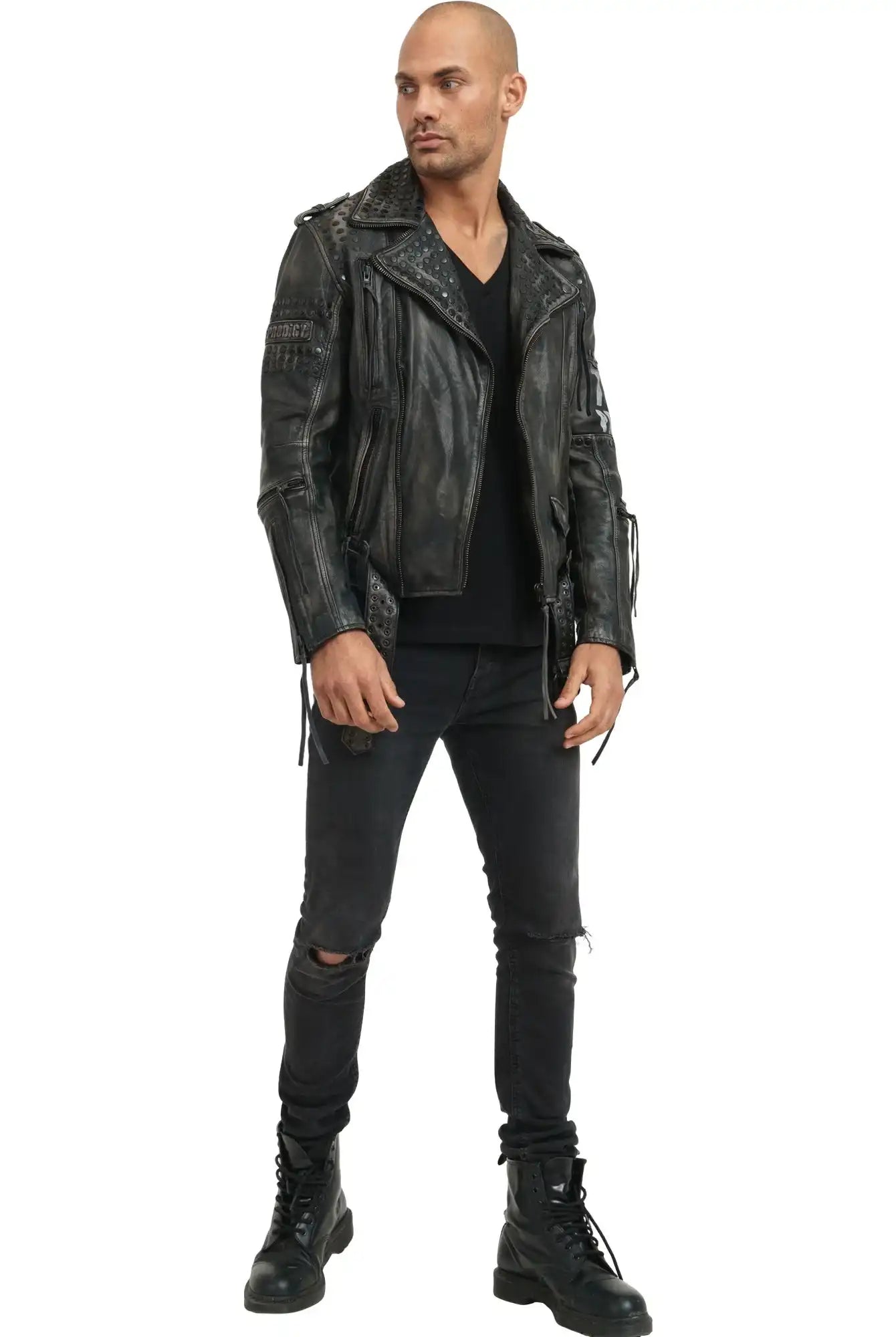 Ein Mann steht mit dem Gesicht nach vorne vor einem weißen Hintergrund. Er trägt die trueprodigy Dwayne Lederjacke mit Nieten und Druck, ein schwarzes Shirt mit V-Ausschnitt, schwarze zerrissene Jeans und schwarze Schnürstiefel mit Nieten-Akzenten.