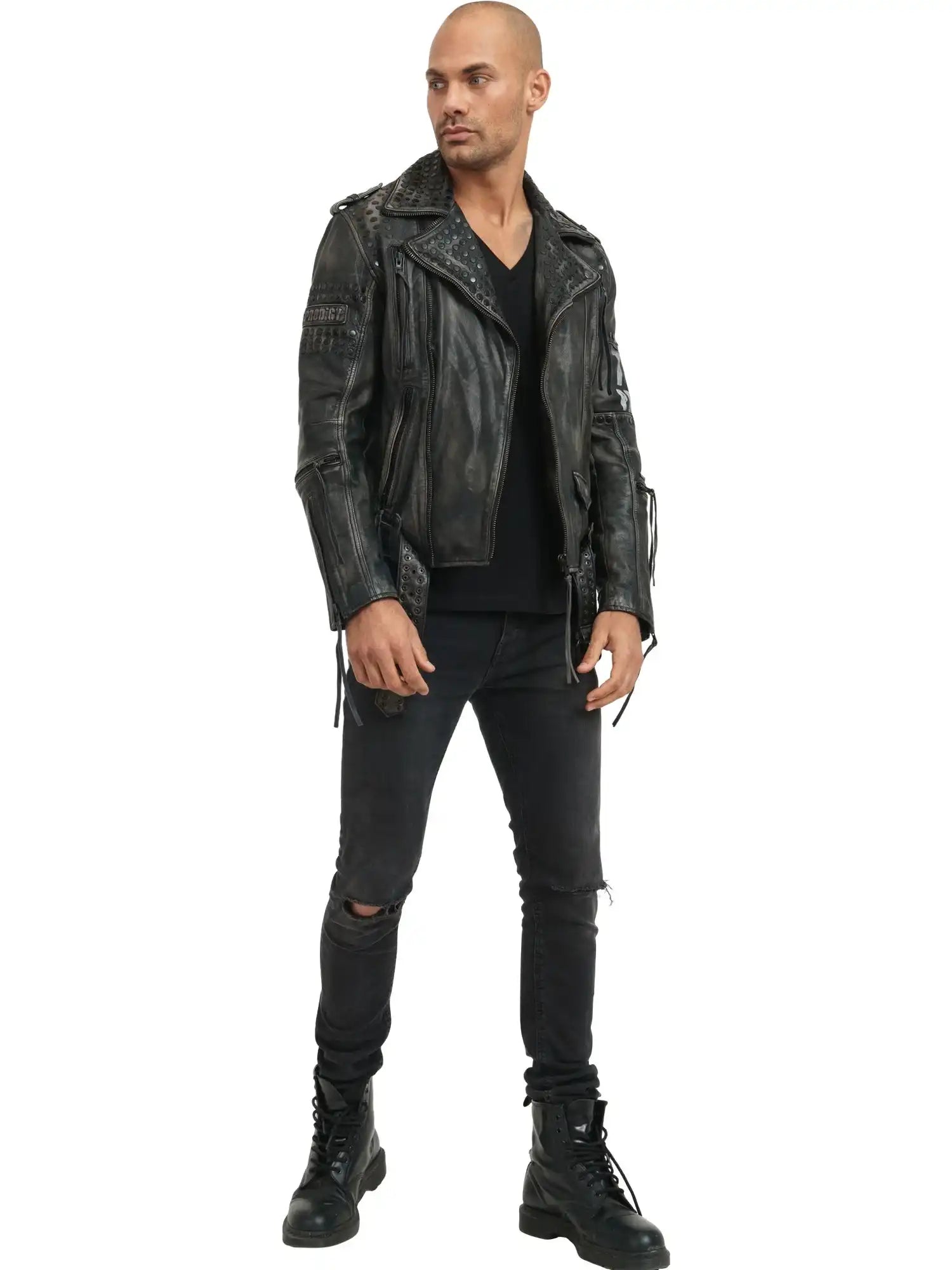 Ein Mann steht mit dem Gesicht nach vorne vor einem weißen Hintergrund. Er trägt die trueprodigy Dwayne Lederjacke mit Nieten und Druck, ein schwarzes Shirt mit V-Ausschnitt, schwarze zerrissene Jeans und schwarze Schnürstiefel mit Nieten-Akzenten.