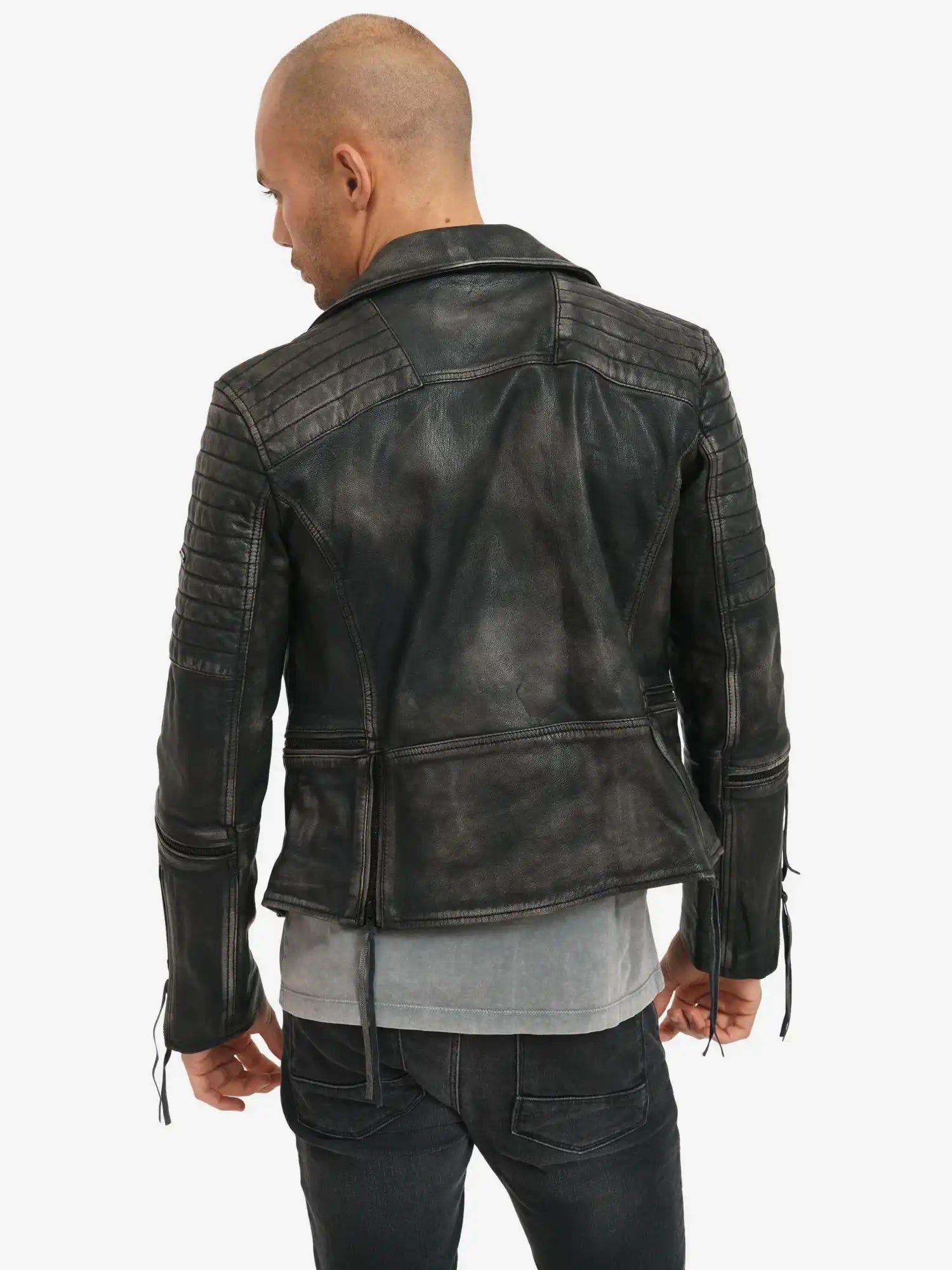 Man sieht eine Person mit rasiertem Kopf von hinten, die die trueprodigy Bryan Lederjacke mit Vintage Optik über einem grauen Hemd und einer dunklen Jeans trägt und vor einem schlichten weißen Hintergrund steht.