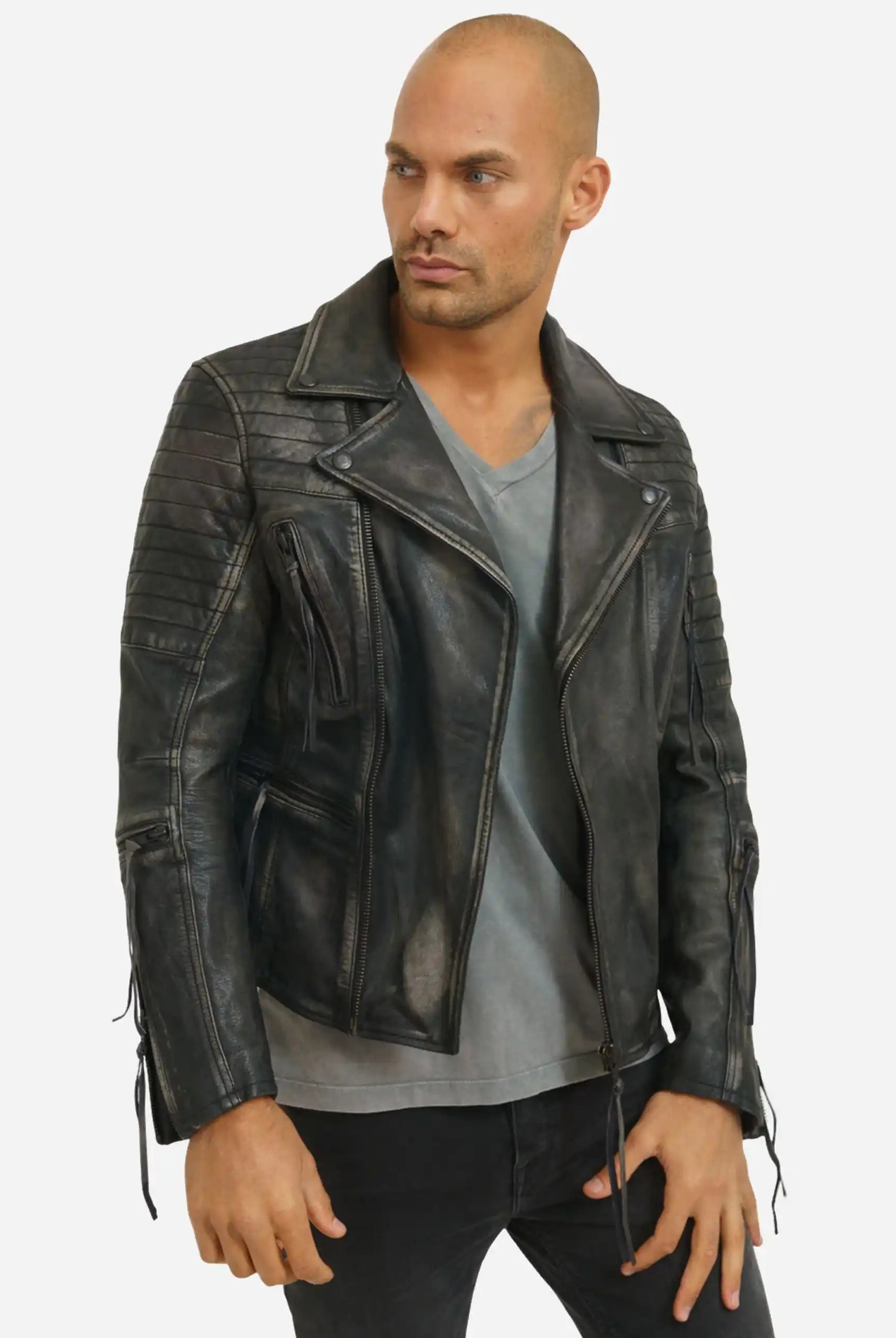 Eine Person steht leicht seitlich und trägt die trueprodigy Bryan Lederjacke mit Vintage Optik über einem grauen T-Shirt und einer schwarzen Hose. Die Jacke verfügt über Reißverschlusstaschen, gesteppte Schultern und geschnürte Manschetten. Der Hintergrund ist einfarbig weiß.