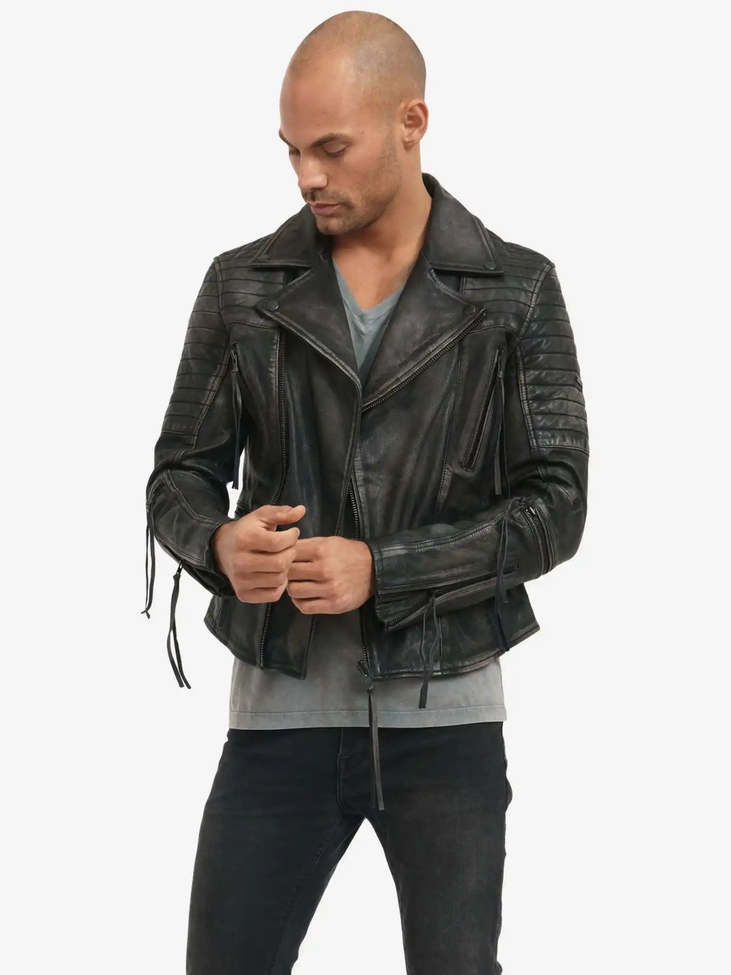 Ein Mann mit rasiertem Kopf trägt die Bryan Lederjacke mit Vintage Optik von trueprodigy über einem grauen T-Shirt und schwarzen Jeans. Er blickt nach unten und justiert den Reißverschluss am Jackenärmel.