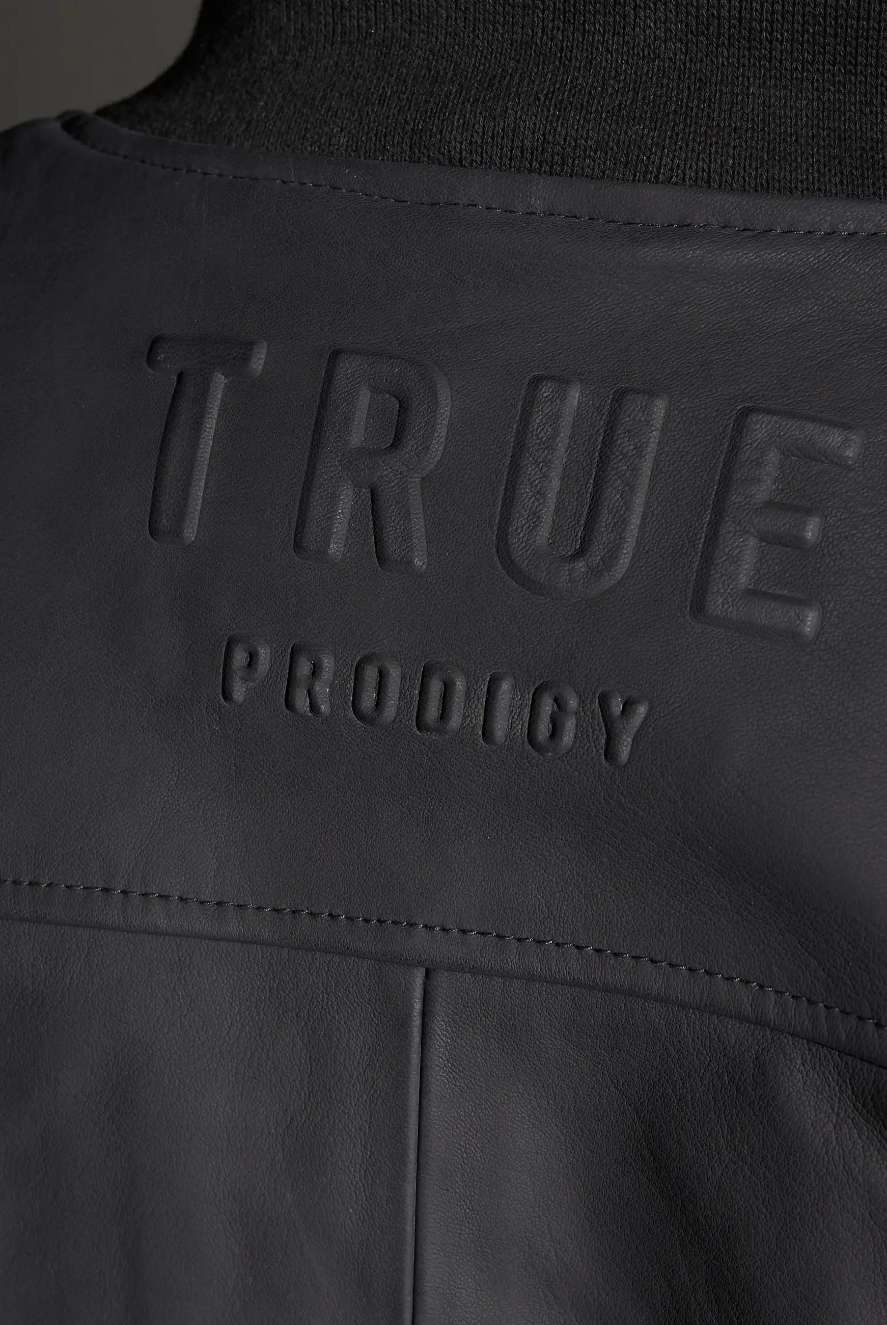 Nahaufnahme einer schwarzen Nazar Oversized Bomber-Lederjacke matt von trueprodigy mit großem, erhabenem trueprodigy-Schriftzug, der quer über den Rücken geprägt ist.