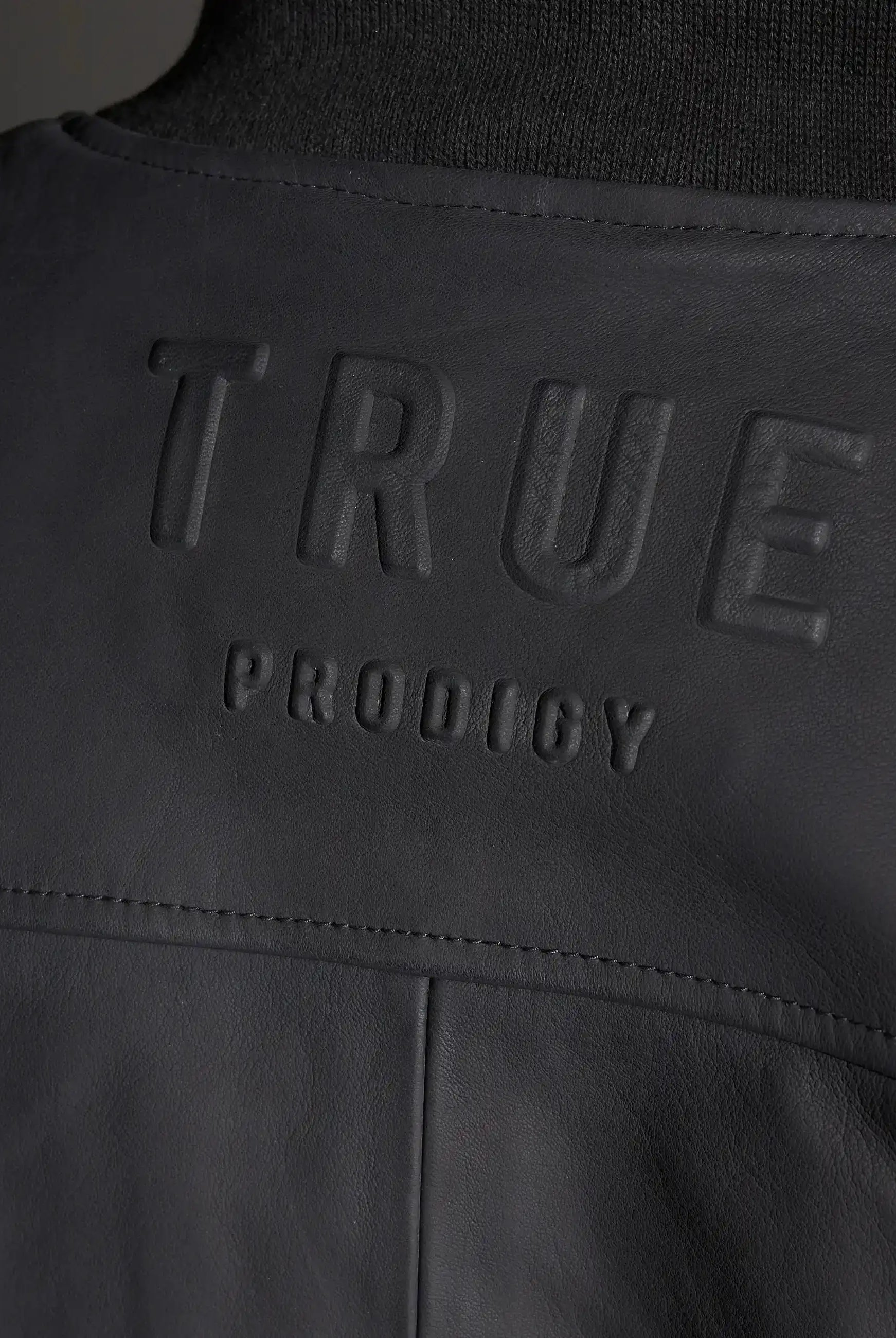 Nahaufnahme einer schwarzen Nazar Oversized Bomber-Lederjacke matt von trueprodigy mit großem, erhabenem trueprodigy-Schriftzug, der quer über den Rücken geprägt ist.