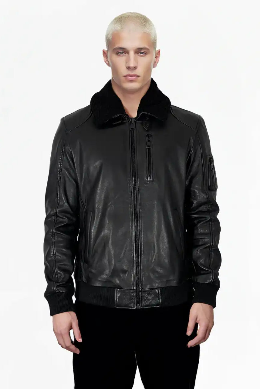 Eine Person mit kurzen, gebleichten blonden Haaren steht mit dem Gesicht nach vorne und trägt die Blaze Moderne Fliegerjacke aus echtem Leder mit abnehmbarem Teddy-Kragen von trueprodigy und eine schwarze Hose vor einem schlichten weißen Hintergrund.