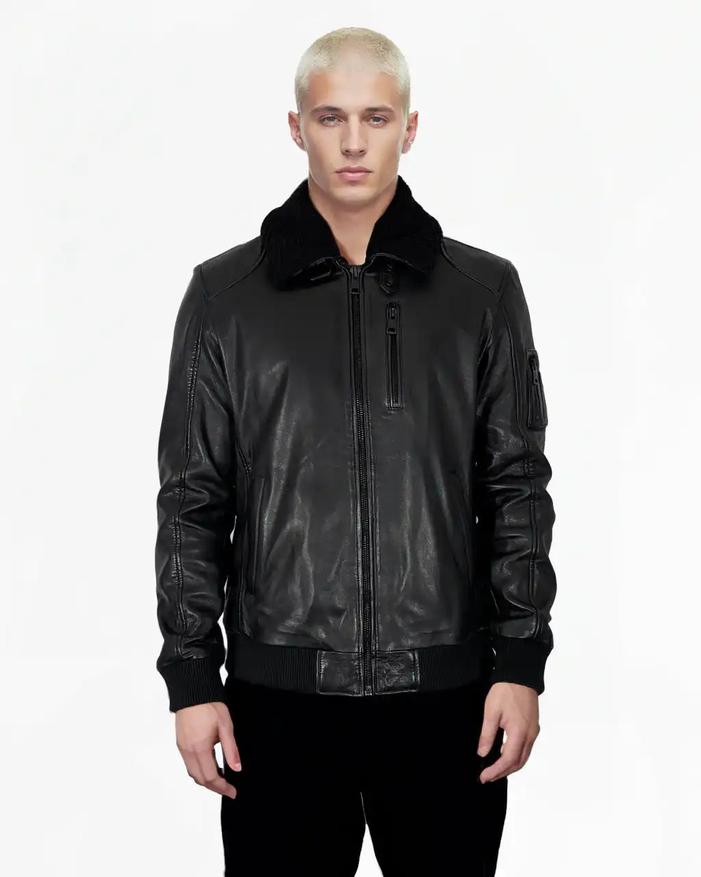 Eine Person mit kurzen, gebleichten blonden Haaren steht mit dem Gesicht nach vorne und trägt die Blaze Moderne Fliegerjacke aus echtem Leder mit abnehmbarem Teddy-Kragen von trueprodigy und eine schwarze Hose vor einem schlichten weißen Hintergrund.