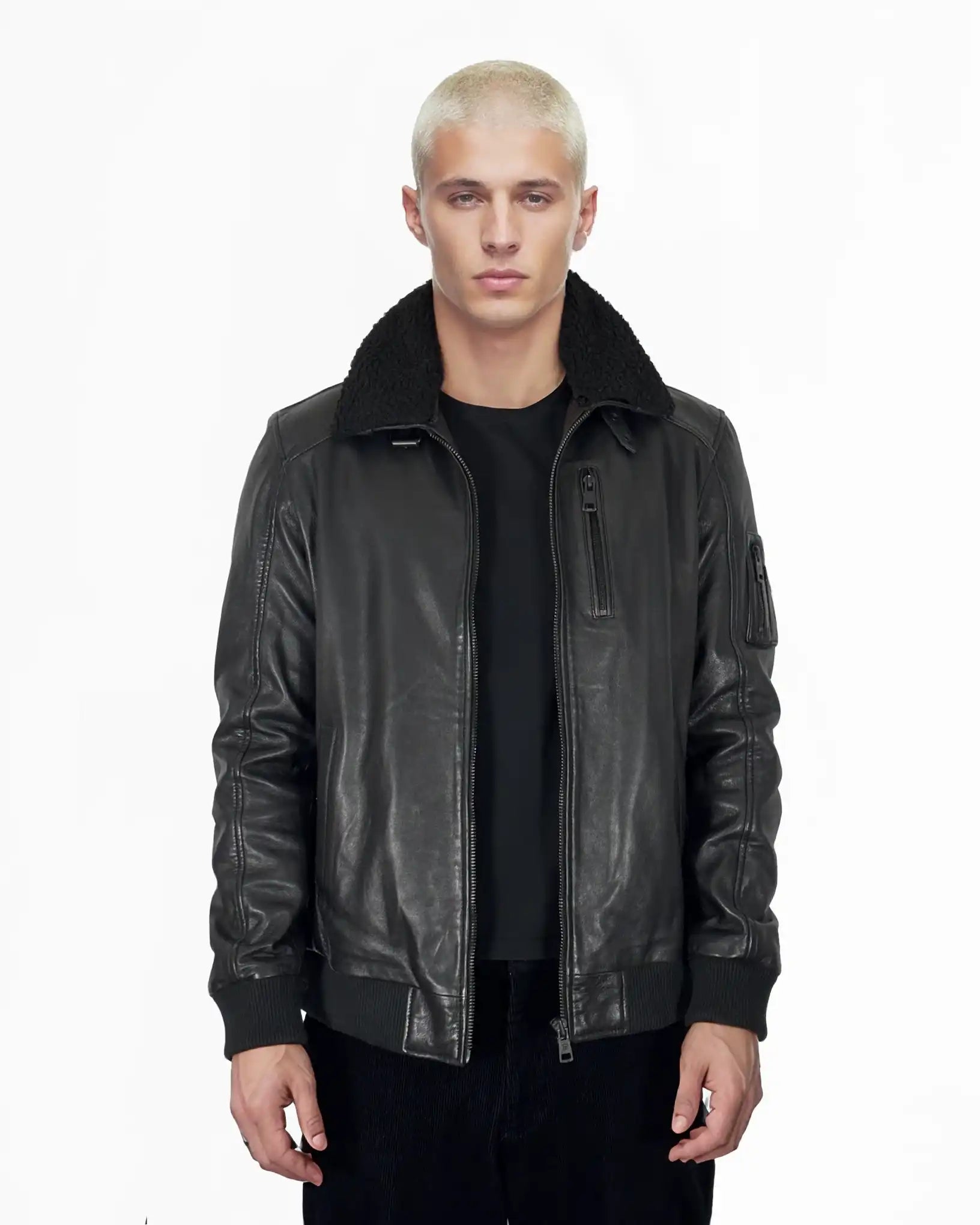 Eine Person mit kurzen, gebleichten blonden Haaren trägt die trueprodigy Blaze Moderne Fliegerjacke aus echtem Leder mit abnehmbarem Teddy-Kragen und ein schwarzes Hemd, stehend vor einem schlichten weißen Hintergrund.