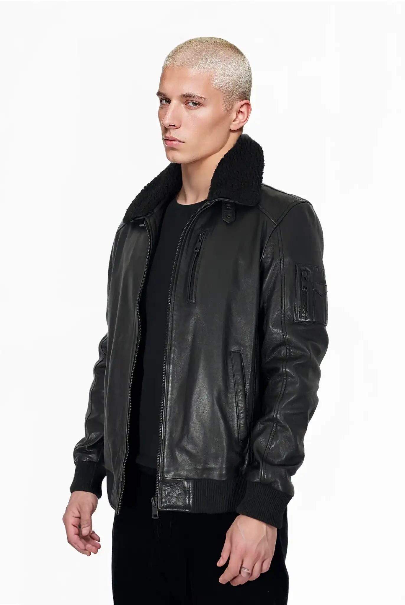 Eine Person mit kurzen, gebleichten blonden Haaren trägt die trueprodigy Blaze Moderne Fliegerjacke aus echtem Leder mit abnehmbarem Teddy-Kragen und schwarzer Hose, steht vor einem schlichten weißen Hintergrund mit den Händen an der Seite und einem neutralen Gesichtsausdruck.