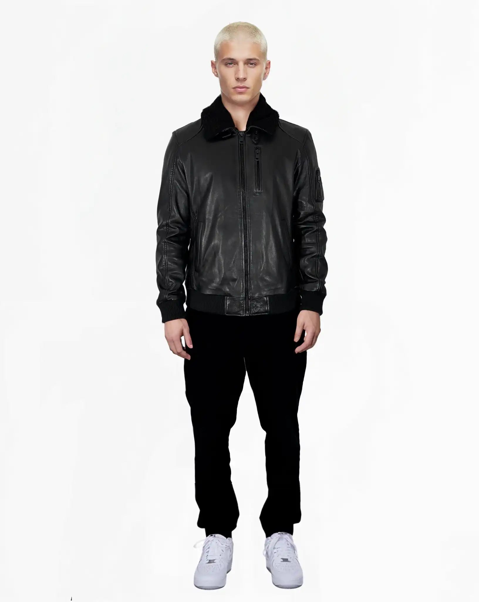 Eine Person mit kurzen blonden Haaren steht vor der Kamera und trägt die Blaze Moderne Fliegerjacke aus echtem Leder mit abnehmbarem Teddy-Kragen von trueprodigy, schwarze Hosen und weiße Sneaker vor einem schlichten weißen Hintergrund.