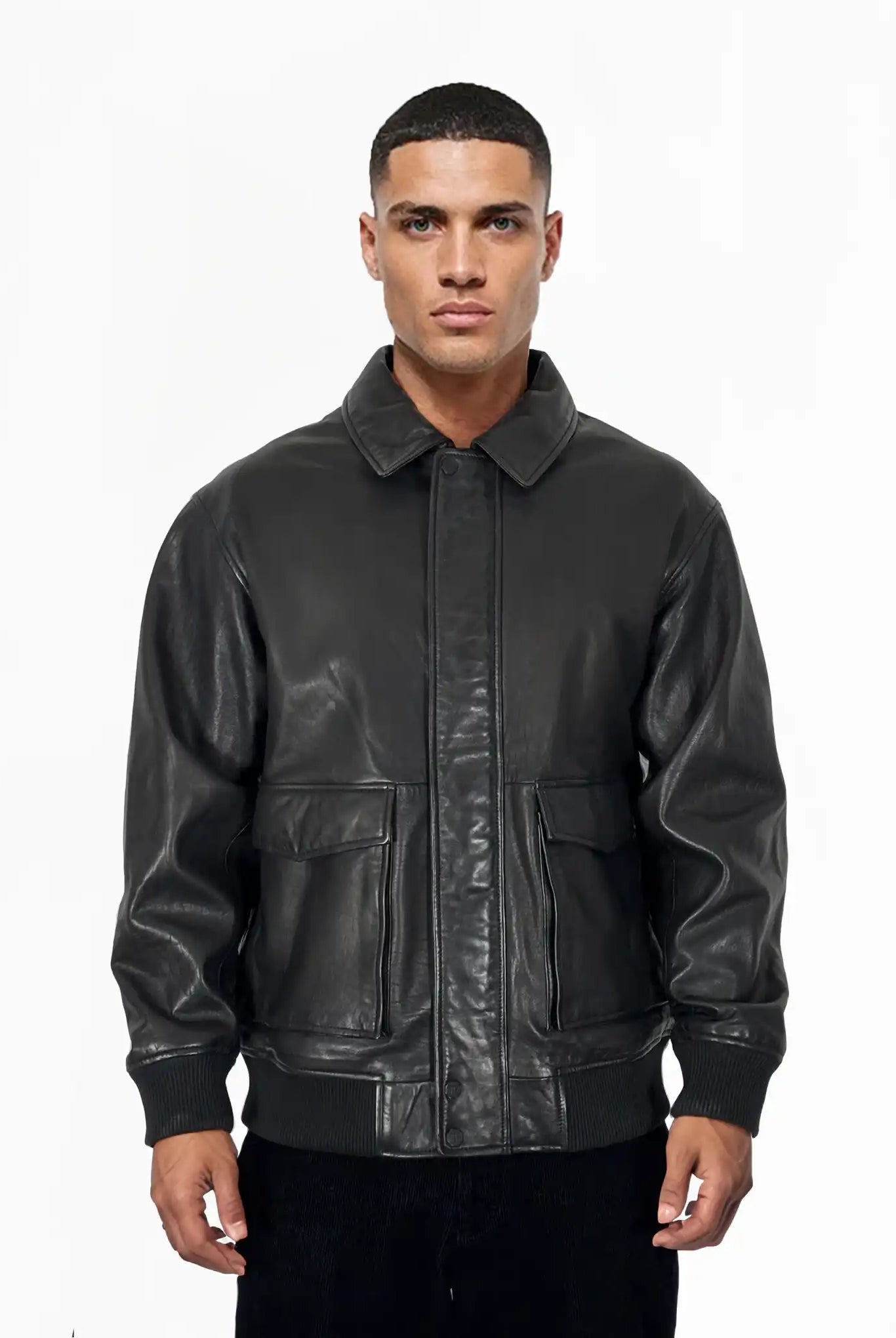 Ein Mann mit kurzen Haaren und neutralem Gesichtsausdruck blickt nach vorne, trägt die trueprodigy Ryder Oversize-Lederjacke mit Stehkragen, 3D-Silikonlogo & Retro-Details und steht vor einem schlichten weißen Hintergrund.