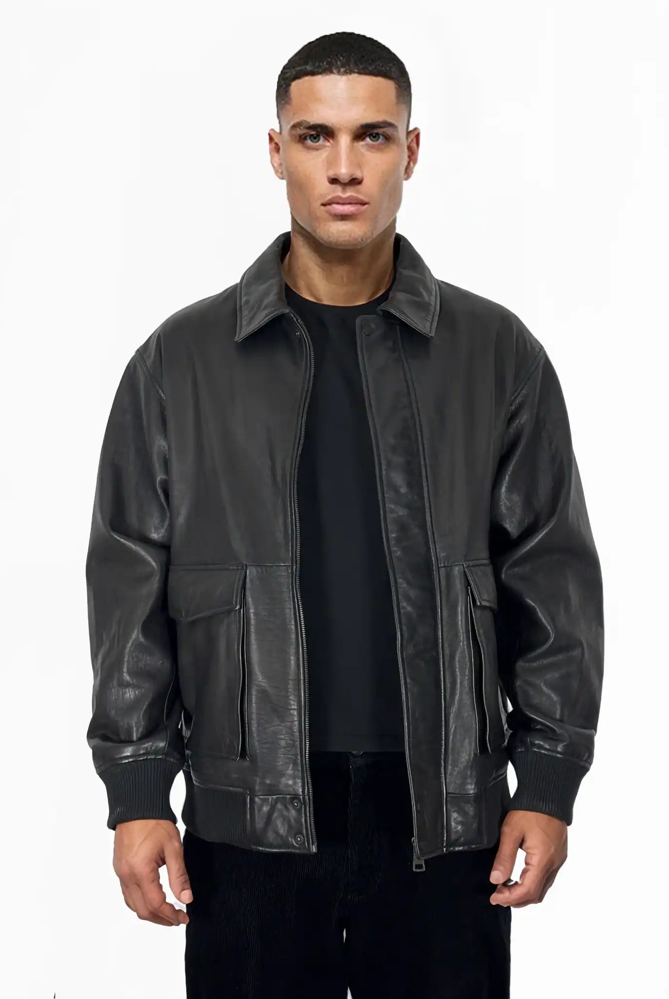 Ein Mann blickt nach vorne, er trägt eine Trueprodigy Ryder Oversize-Lederjacke mit Stehkragen, 3D-Silikonlogo & Retro-Details über einem schwarzen Hemd und einer Hose, vor einem schlichten weißen Hintergrund.