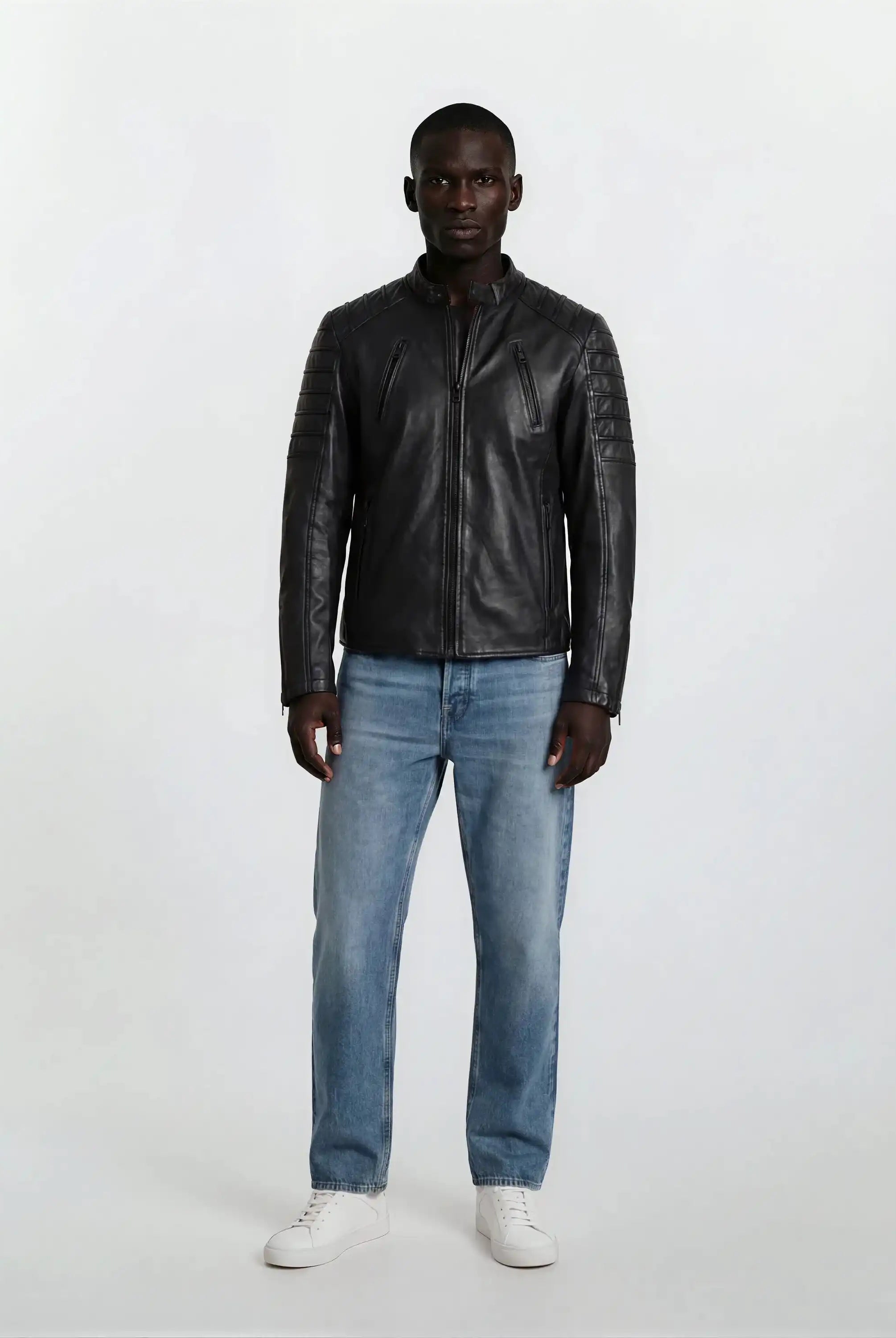 Eine Person steht mit dem Gesicht nach vorne vor einem schlichten weißen Hintergrund und trägt eine trueprodigy Slim-Fit-Lederjacke mit Stehkragen & Zipper-Details, hellblaue Jeans und weiße Turnschuhe.