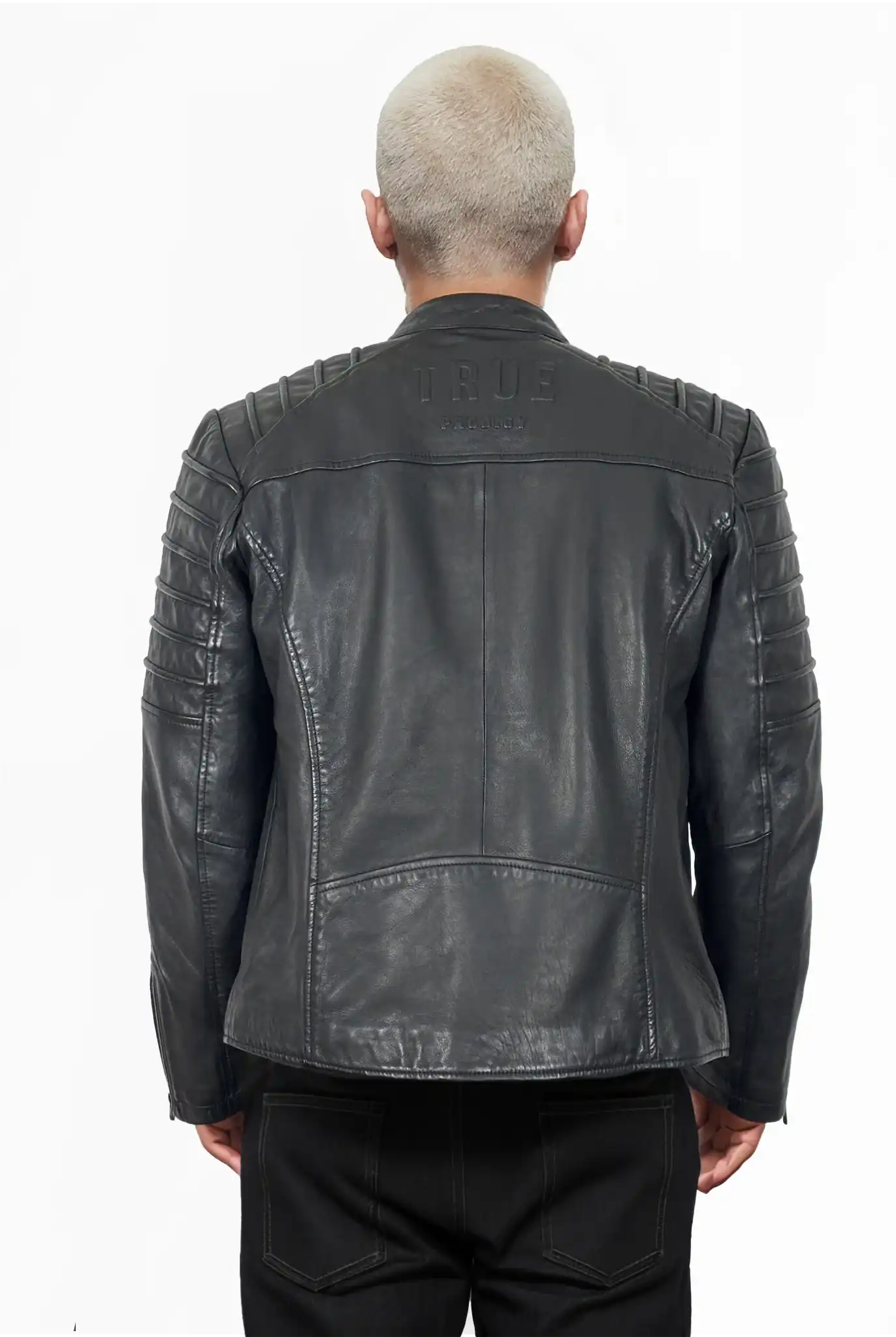 Eine Person mit kurzgeschnittenen, hellen Haaren trägt von hinten die schwarze Dash Slim-Fit-Lederjacke mit Stehkragen & Zipper-Details von trueprodigy, mit abgesteppten Schulter- und Armdetails und "TRUE"-Prägung auf dem oberen Rücken.