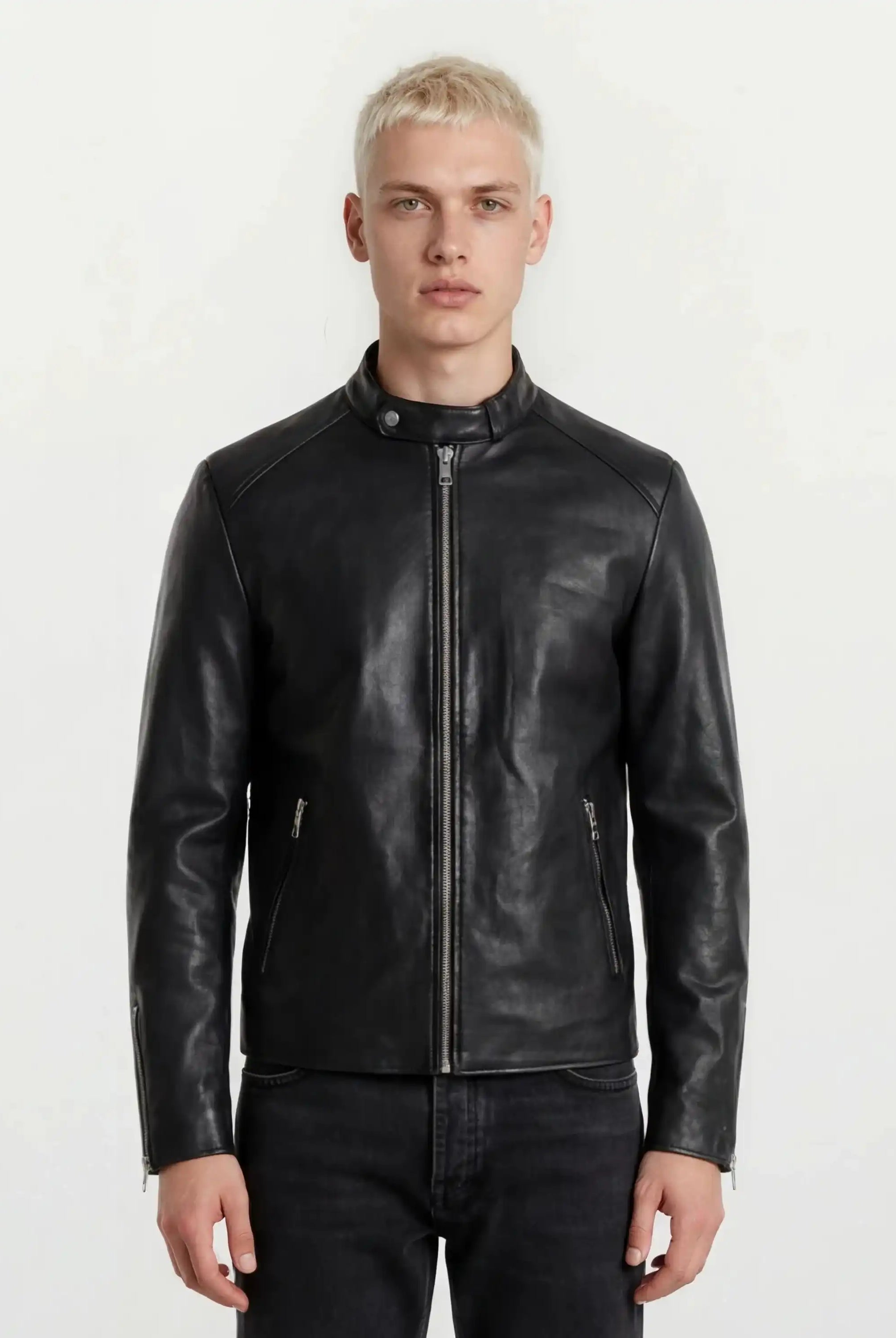 Eine Person mit kurzen blonden Haaren trägt die trueprodigy Slim-Fit-Lederjacke mit sichtbarem 3D-Rückenlogo und schwarze Jeans, steht vor einem schlichten weißen Hintergrund und blickt in die Kamera.