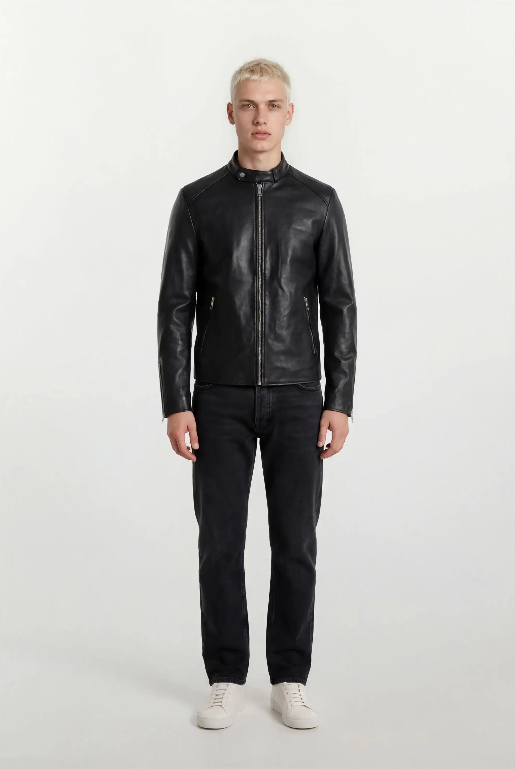 Eine Person mit kurzen blonden Haaren steht mit dem Gesicht nach vorne und trägt eine trueprodigy Slim-Fit-Lederjacke mit sichtbarem 3D-Rückenlogo, dunkle Jeans und weiße Turnschuhe vor einem schlichten weißen Hintergrund.