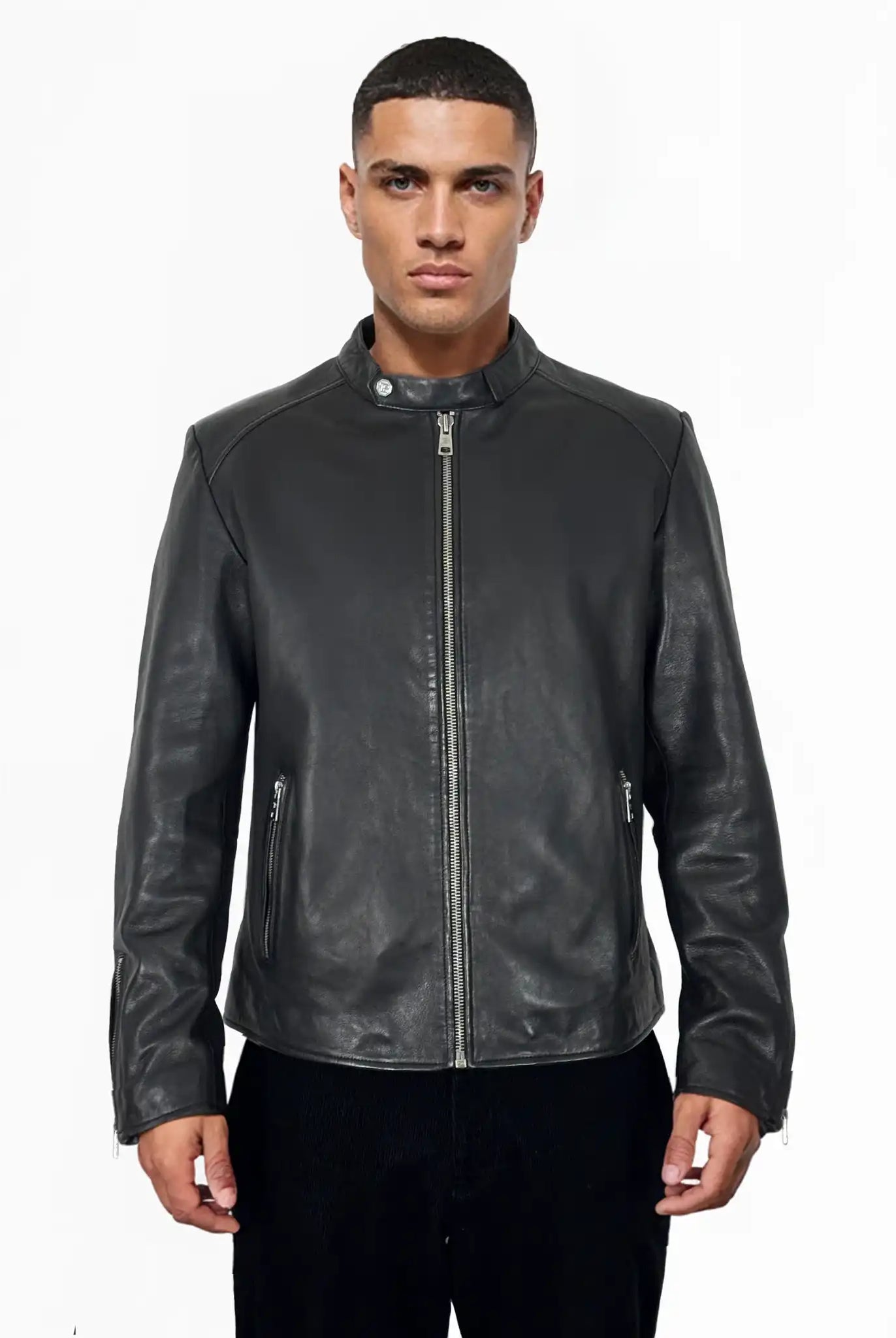 Eine Person steht vor der Kamera und trägt die trueprodigy Jonas Slim-Fit-Lederjacke mit sichtbarem 3D-Rückenlogo mit Frontreißverschluss und Reißverschlusstaschen, gepaart mit einer schwarzen Hose, vor einem schlichten weißen Hintergrund.