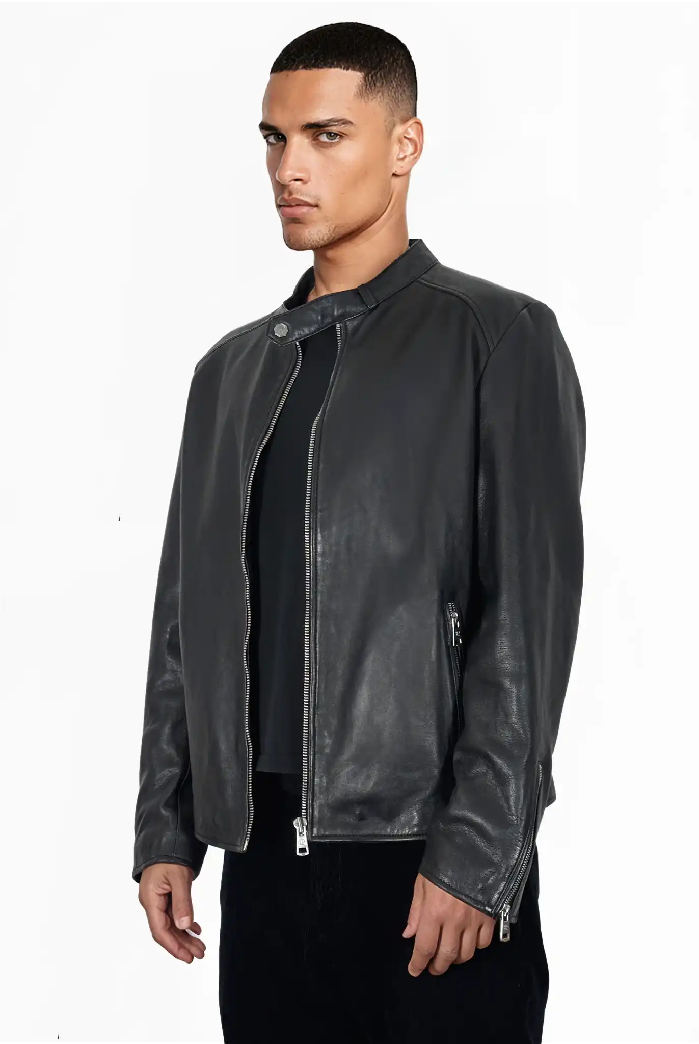 Ein Mann mit kurzen Haaren trägt die trueprodigy Jonas Slim-Fit-Lederjacke mit sichtbarem 3D-Rückenlogo über einem schwarzen Hemd und einer dunklen Hose, steht vor einem schlichten weißen Hintergrund und schaut leicht zur Seite.