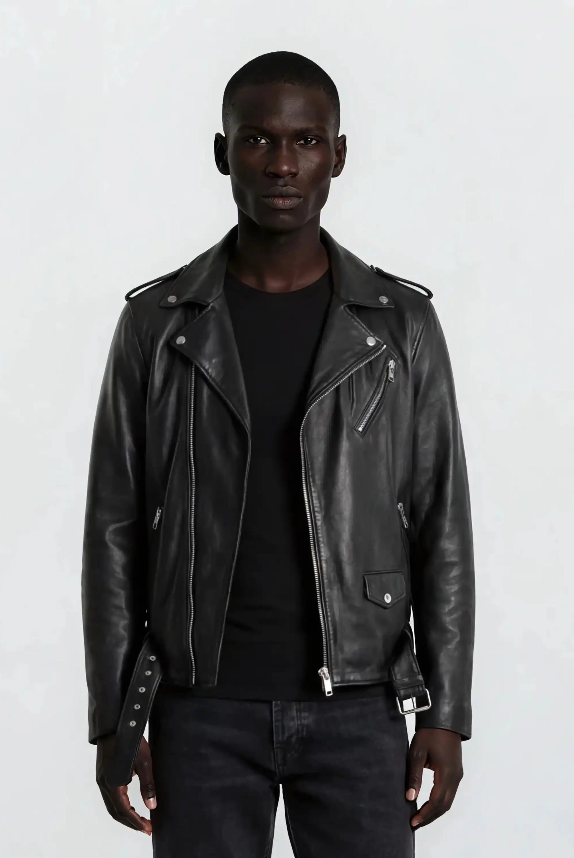 Eine Person blickt in die Kamera und trägt eine trueprodigy Leder-Bikerjacke mit asymmetrischem Zipper & 3D-Logo unter dem Kragen über einem schwarzen Hemd und einer dunklen Jeans vor einem schlichten hellgrauen Hintergrund.