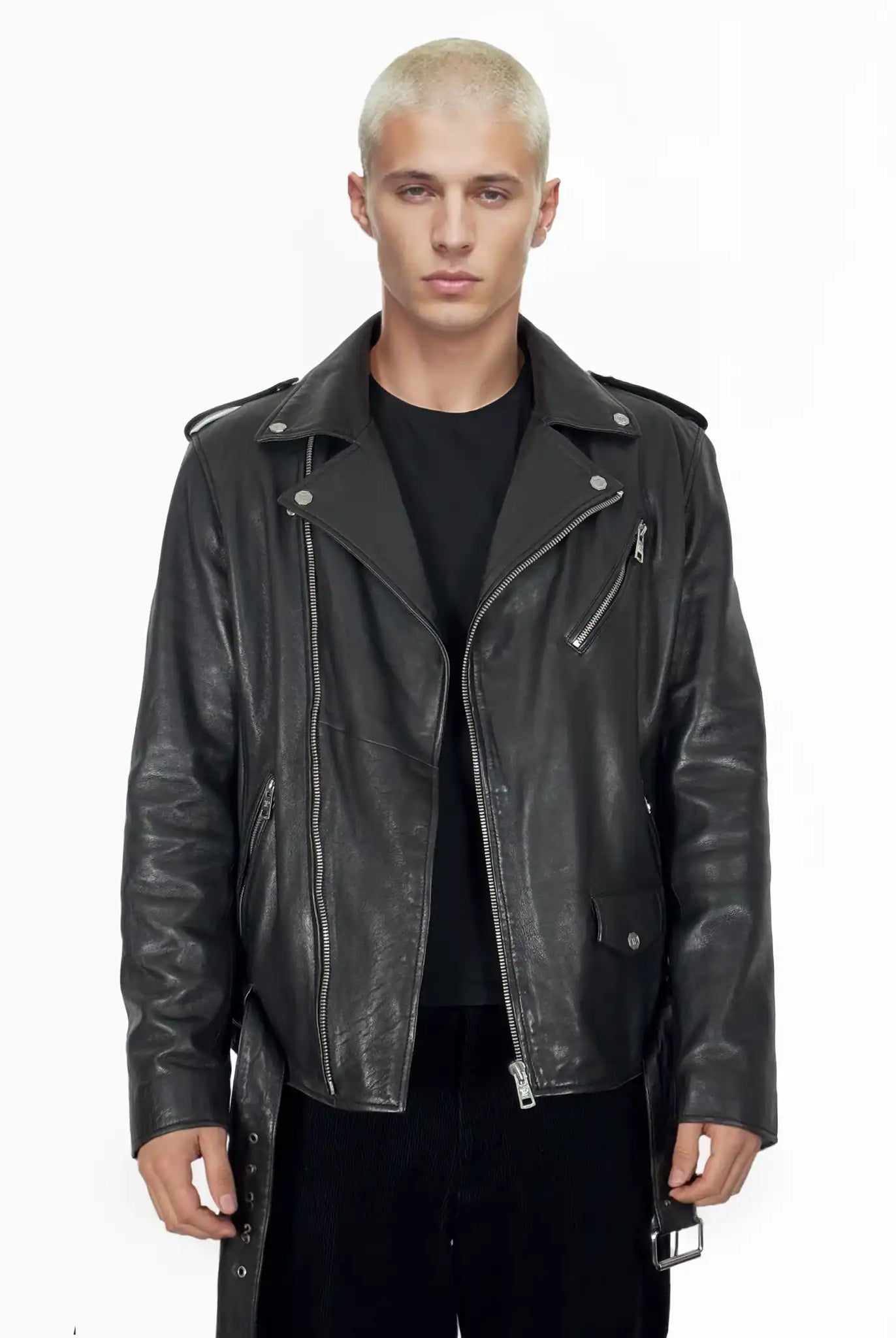 Eine Person mit kurzen, platinblonden Haaren trägt die trueprodigy Easton Leder-Bikerjacke mit asymmetrischem Reißverschluss und 3D-Logo unter dem Kragen über einem schwarzen Hemd und einer Hose vor einem schlichten weißen Hintergrund. Die Jacke hat Reißverschlüsse, Aufschläge und Knopfdetails.