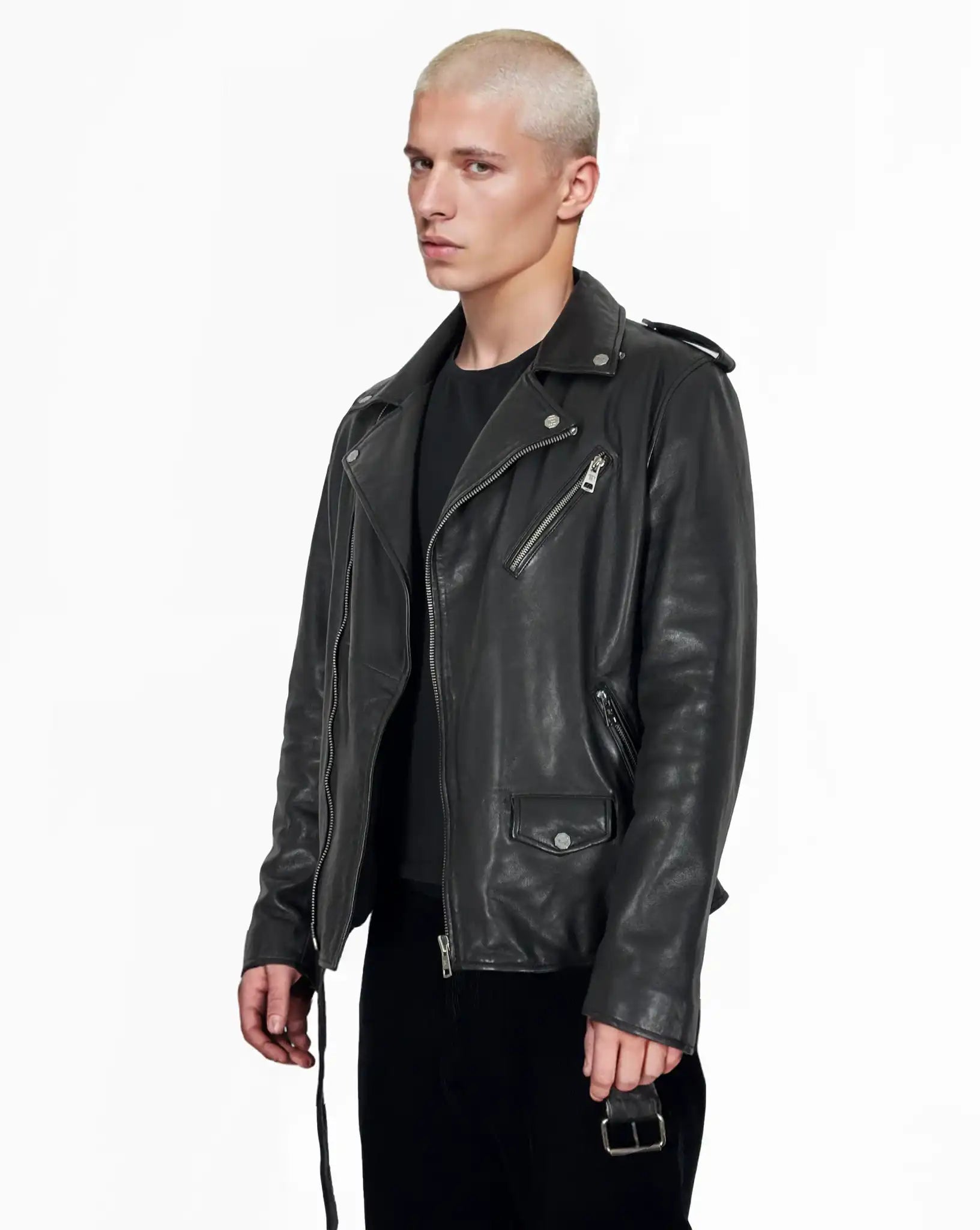 Eine Person mit kurzen, gebleichten blonden Haaren trägt eine trueprodigy Easton Leder-Bikerjacke mit asymmetrischem Zipper & 3D-Logo unter dem Kragen über einem schwarzen Hemd und einer Hose, stehend vor einem schlichten weißen Hintergrund.