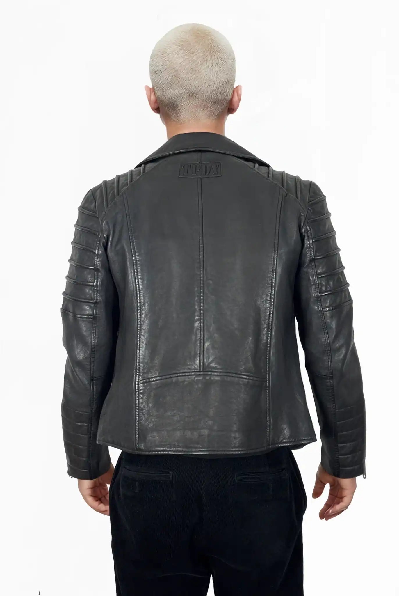 Eine Person mit kurzen, hellen Haaren ist von hinten zu sehen. Sie trägt die trueprodigy John Jacke mit gesteppten Schulter- und Armdetails, gepaart mit einer schwarzen Hose vor einem weißen Hintergrund.