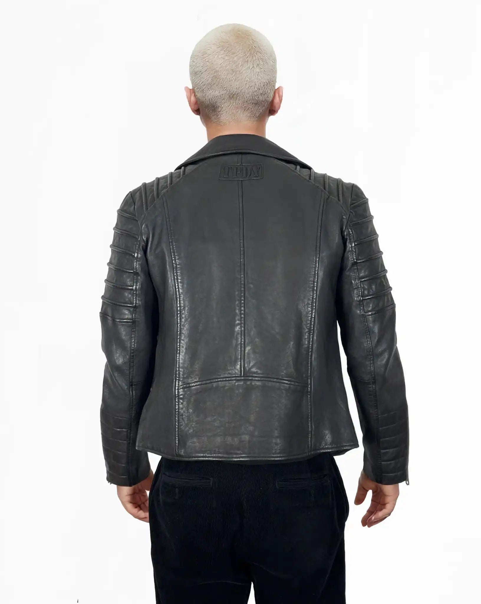 Eine Person mit kurzen, hellen Haaren ist von hinten zu sehen. Sie trägt die trueprodigy John Jacke mit gesteppten Schulter- und Armdetails, gepaart mit einer schwarzen Hose vor einem weißen Hintergrund.