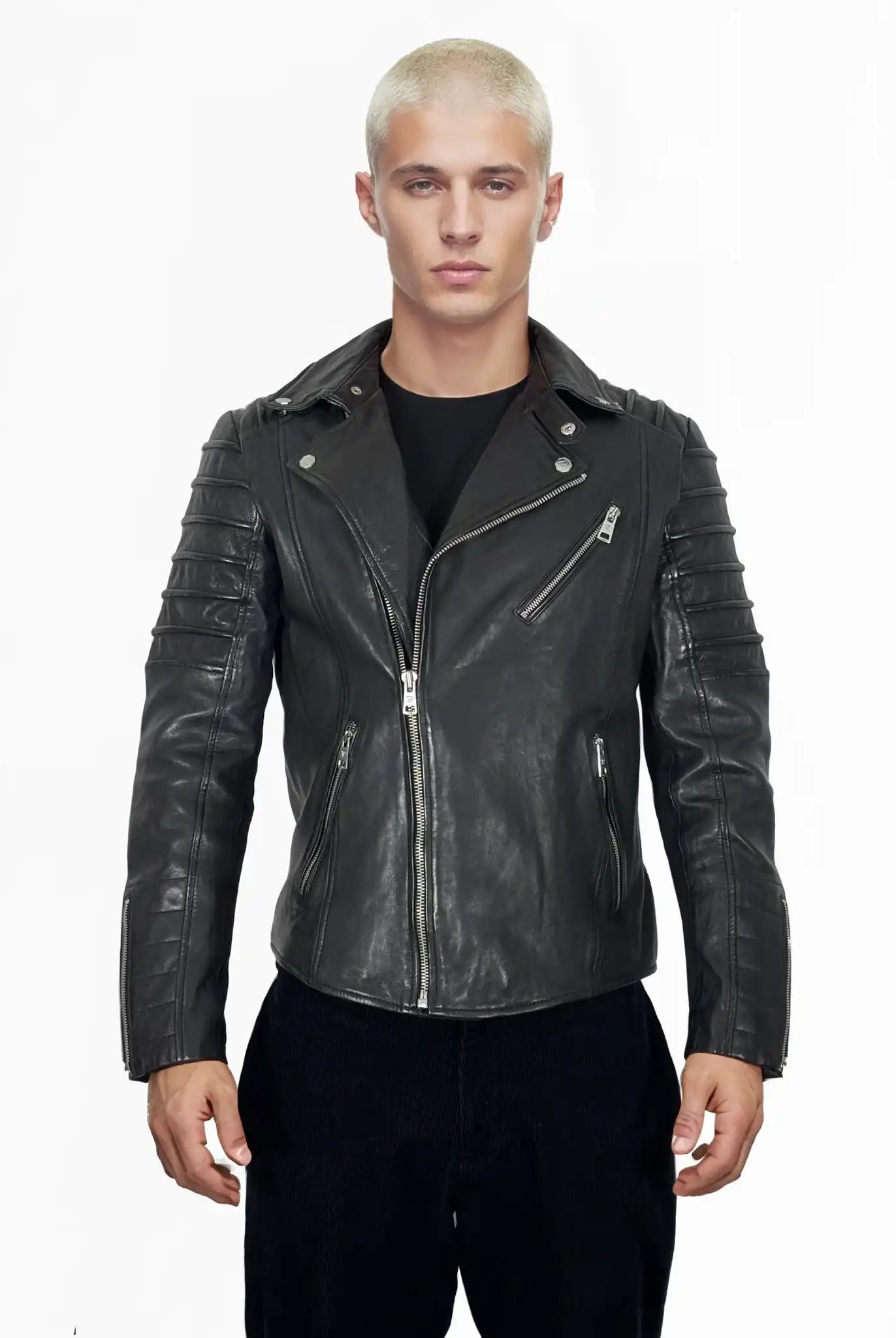 Eine Person mit kurzen, gebleichten blonden Haaren blickt nach vorne, trägt die Jacke John von trueprodigy über einem schwarzen Hemd und einer schwarzen Hose und steht vor einem schlichten weißen Hintergrund.