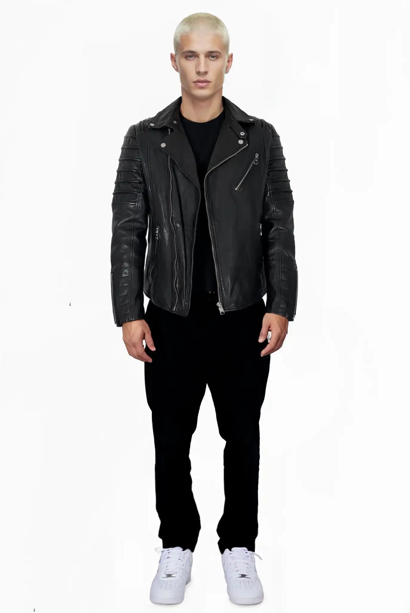 Eine Person mit kurzen blonden Haaren steht vor einem weißen Hintergrund und trägt die John schwarze Schafsleder Jacke von trueprodigy, zusammen mit einer schwarzen Hose, einem schwarzen Hemd und weißen Sneakers.